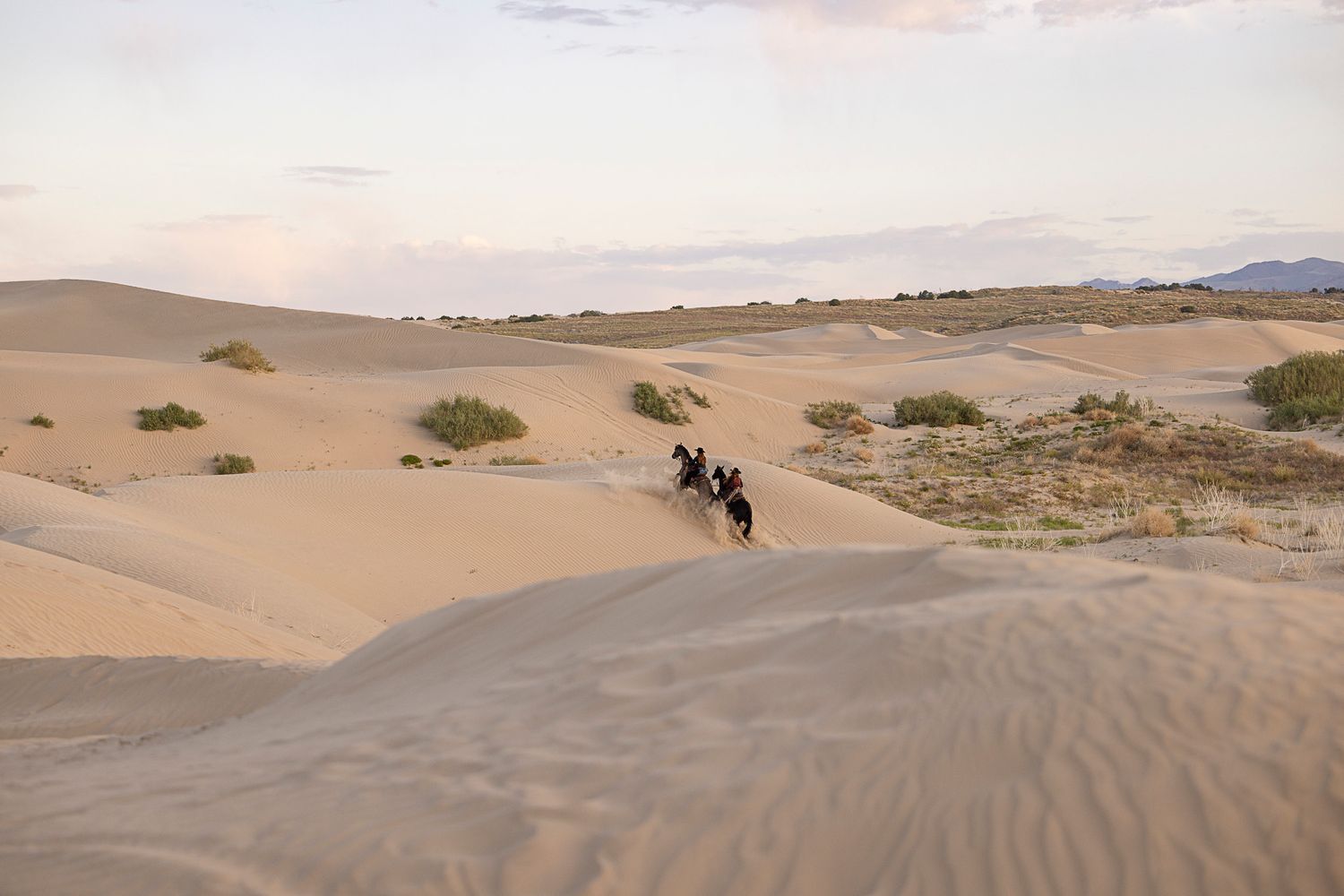 Two riders traversing through the Little Sahara Sand Dunes with a soft sunrise