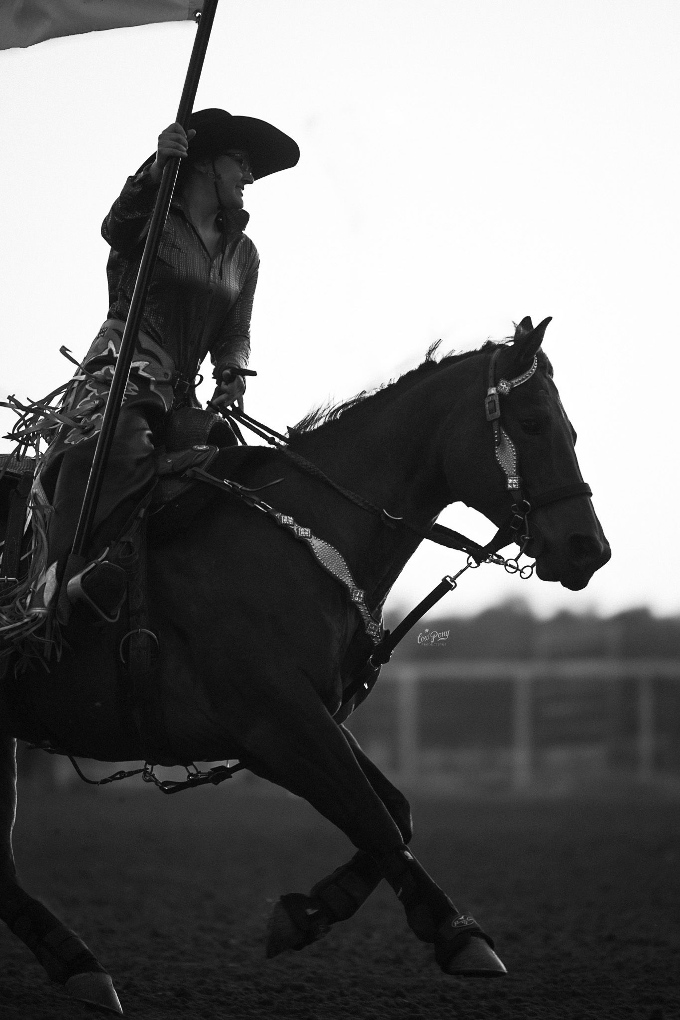 A silhouetted cowgirl rides a horse in dramatic black and white, capturing the motion of western horsemanship.
