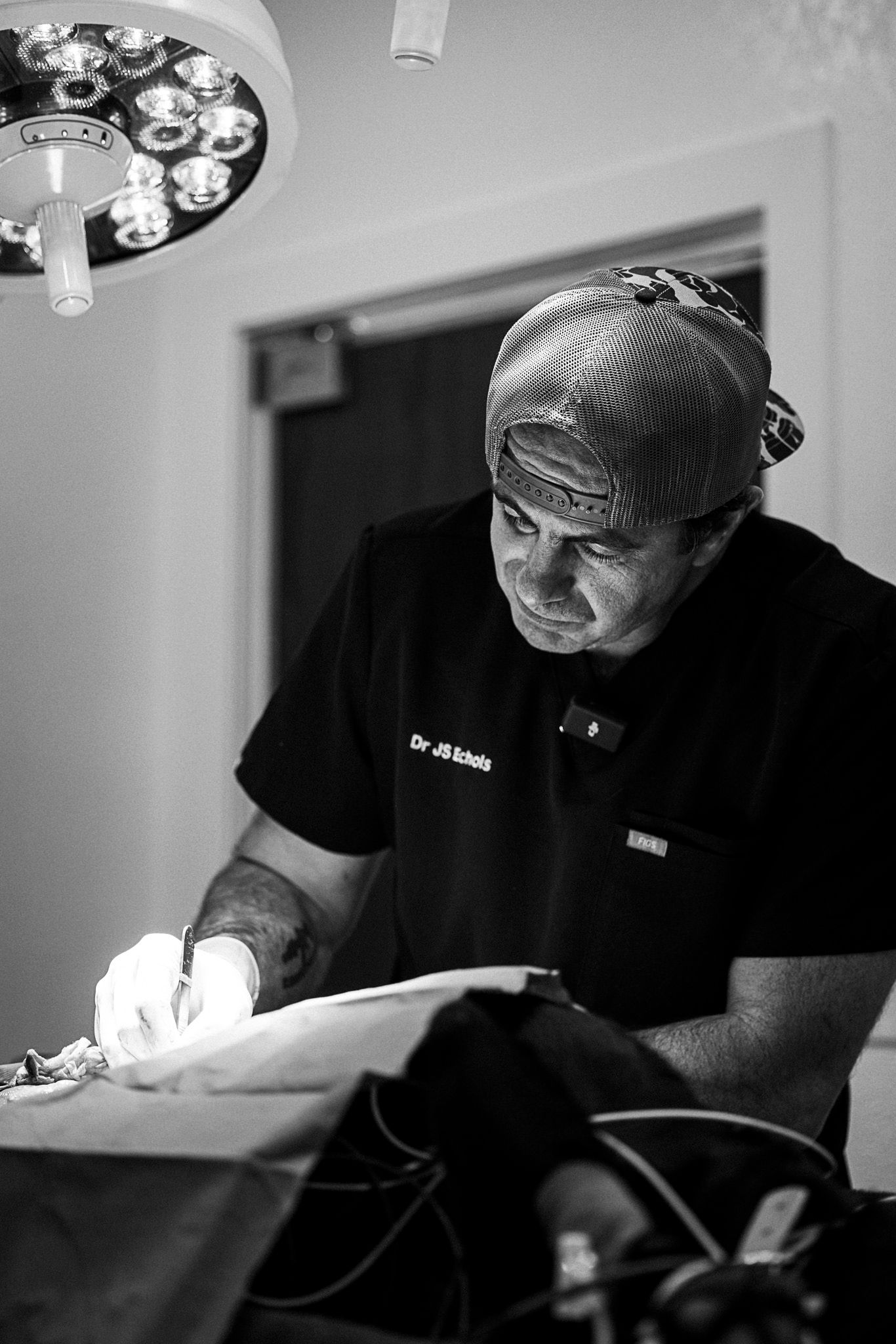 Black and white photo of a veterinary professional in protective gear performing a procedure under surgical lighting.