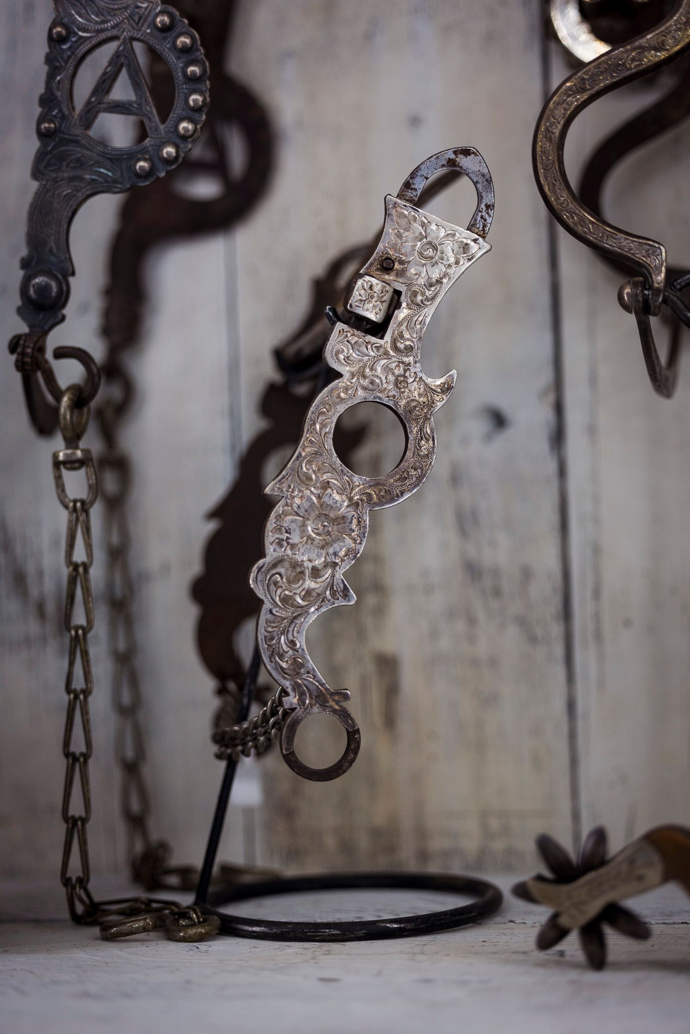 Ornate silver western horse bit with intricate floral engraving on a display