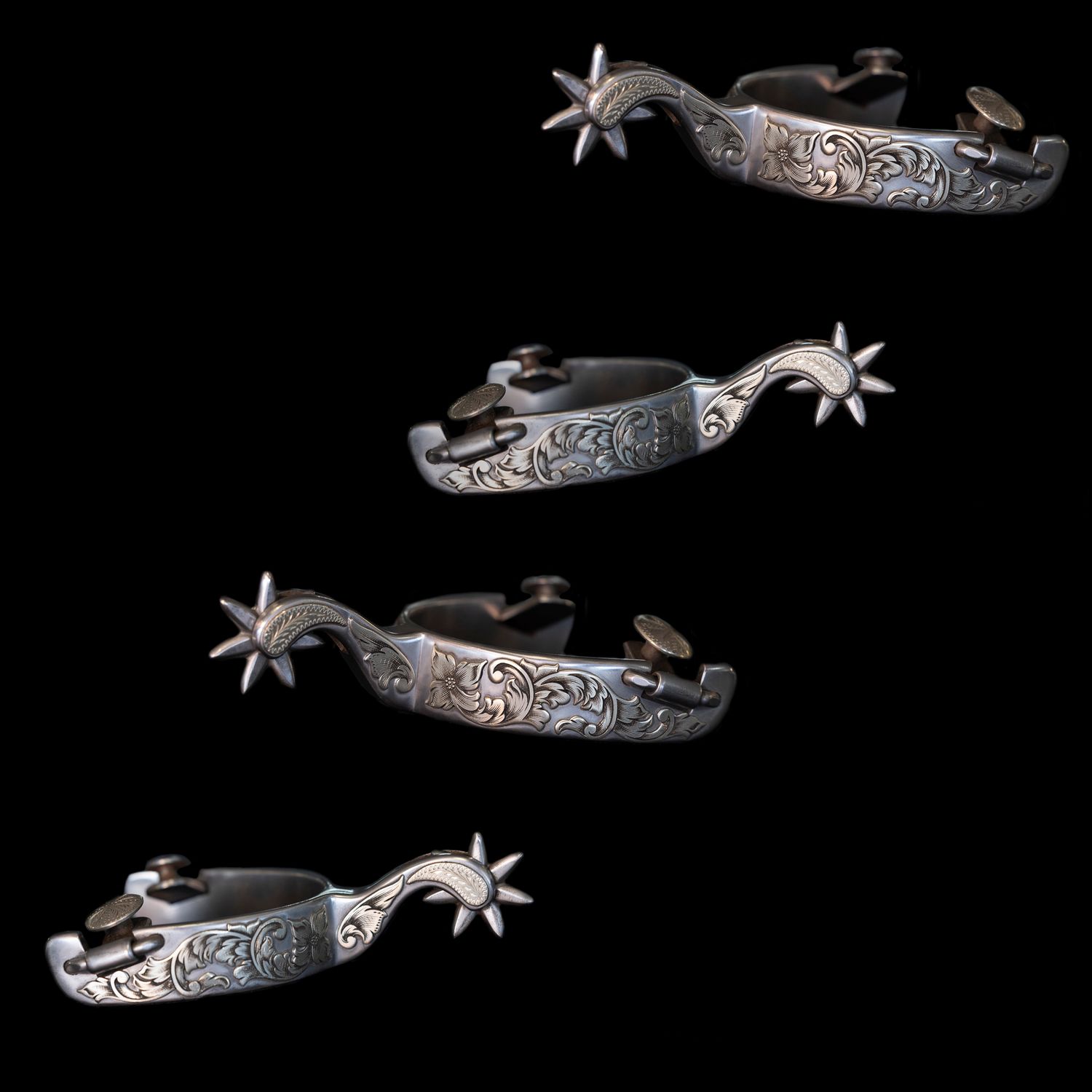 Silver cowboy spurs with engraved decorative patterns and star-shaped rowels displayed on black background.