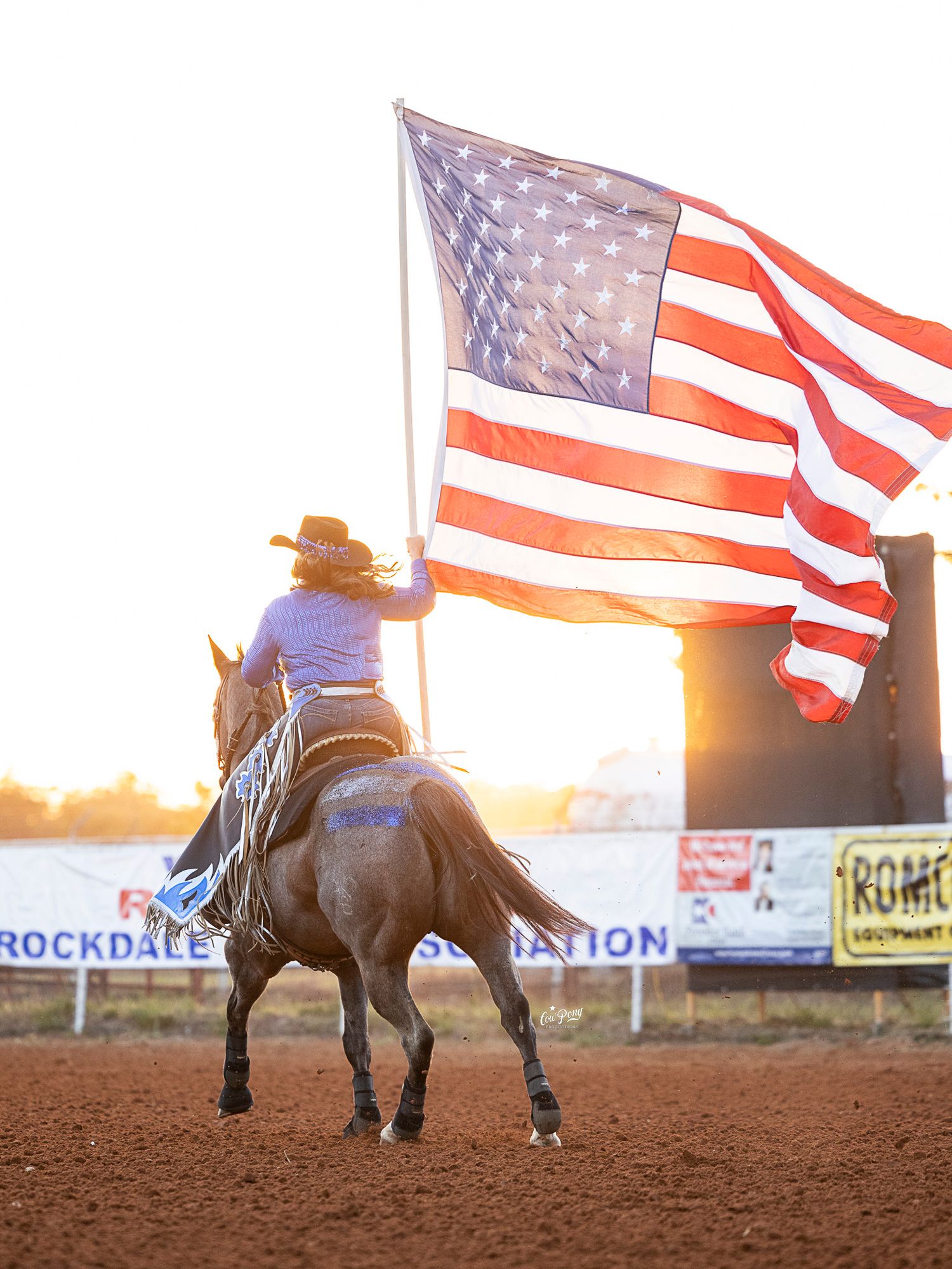 A rider on horseback carries the American flag during a rodeo at sunset in Rockdale, Texas.