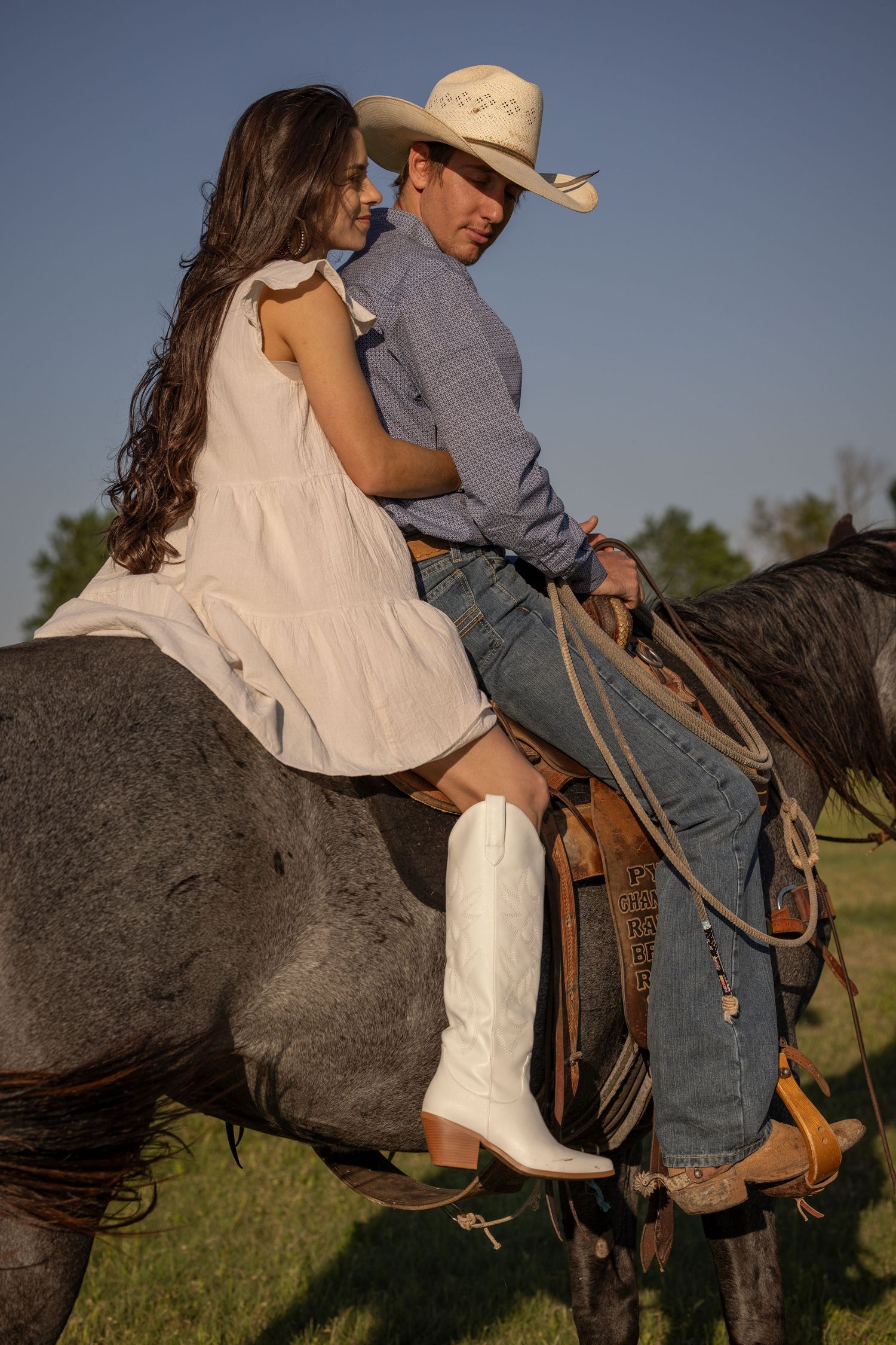 A romantic western-style scene with two people sharing an intimate moment while sitting together on a blue roan horse at sunset.