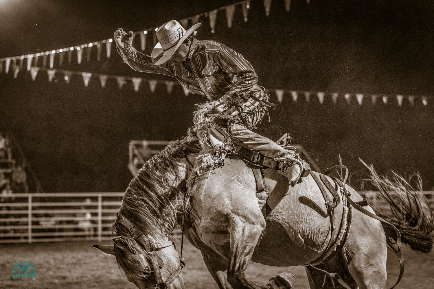 vintage looking photo of a saddle bronc rider at the Teague 4th of July Rodeo with festive flags hanging in the background