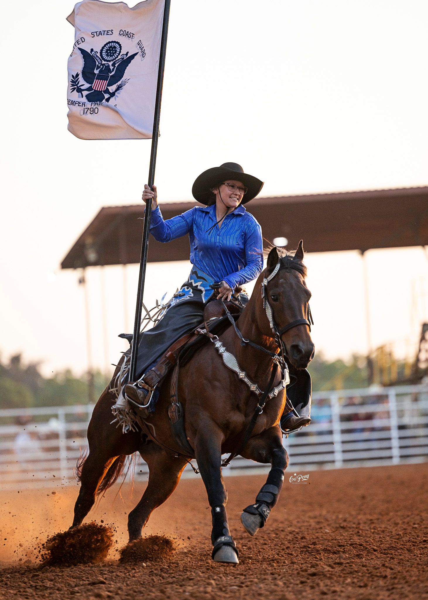 A cowgirl on a bay horse galloping while carrying a flag at a rodeo.