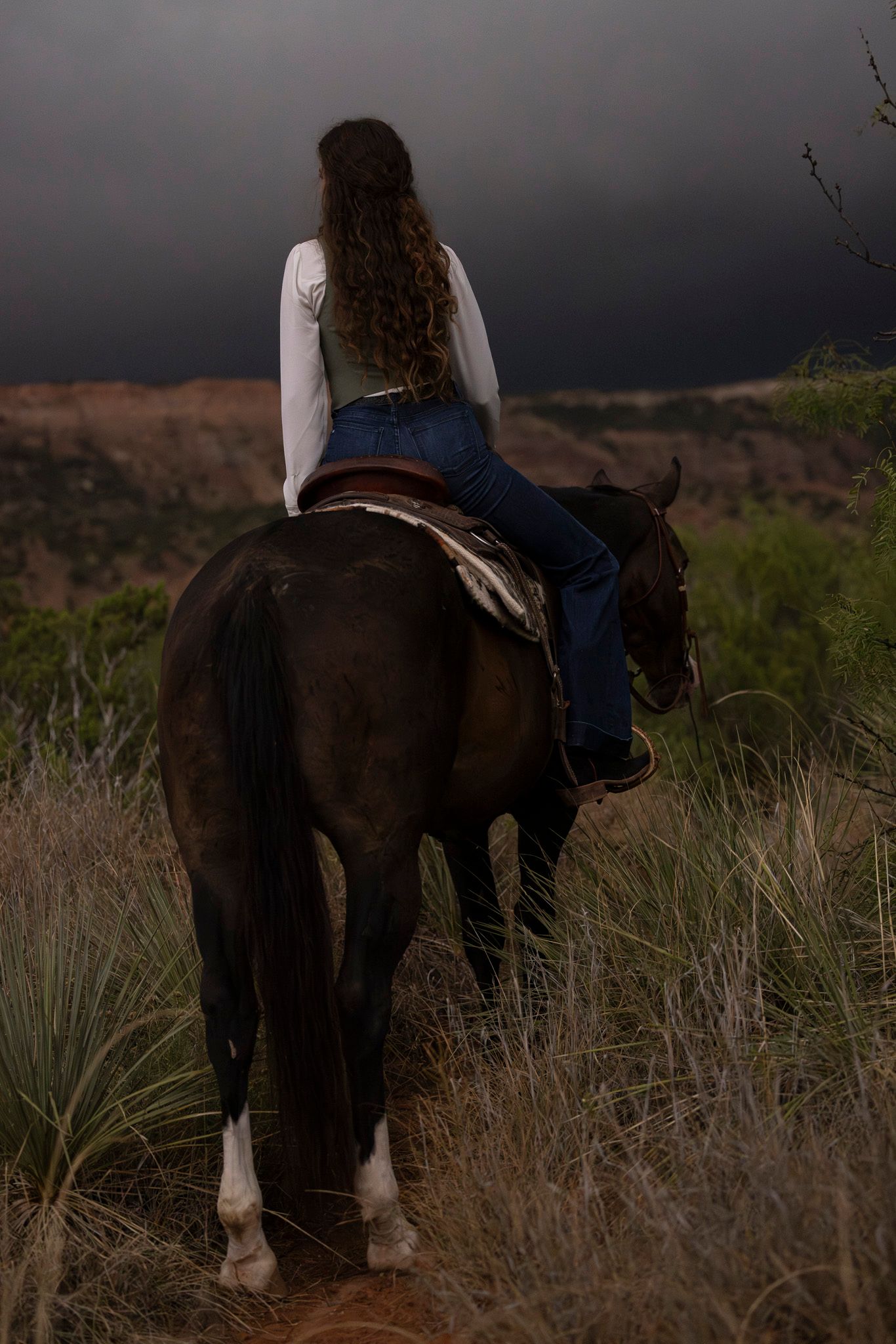 A cowgirl on a bay horse as a thunderstorm is rolling into the Palo Duro Canyon State Park