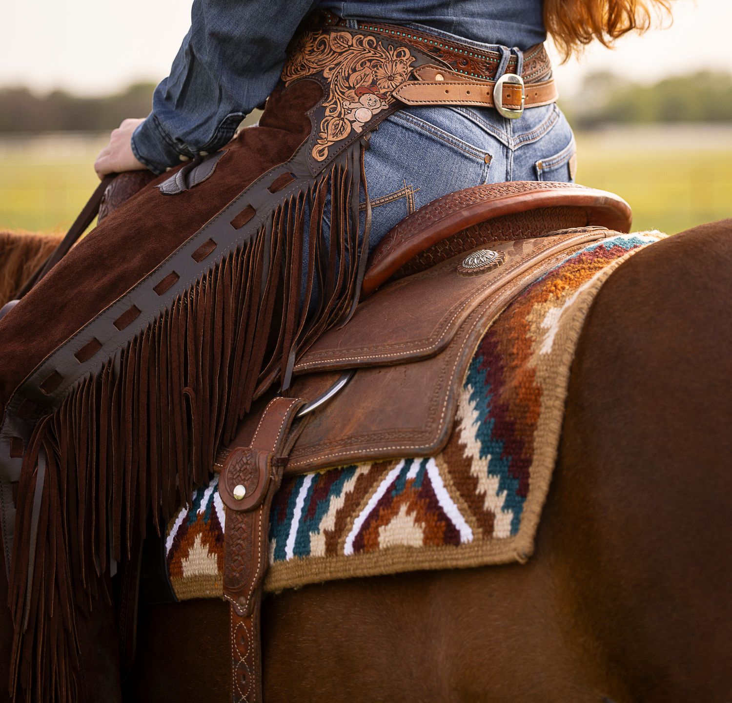 close up of a rider on a horse wearing a pair of custom chaps hand tooled by FS Ranch Designs