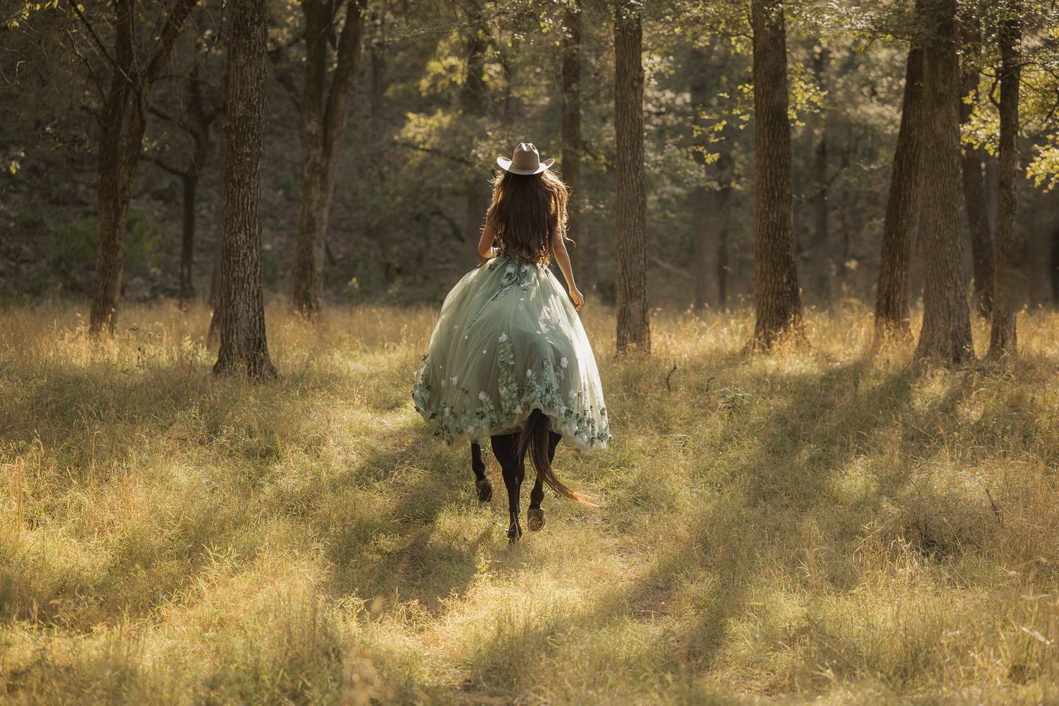 A figure in a flowy dress rides horseback through a sunlit forest clearing.