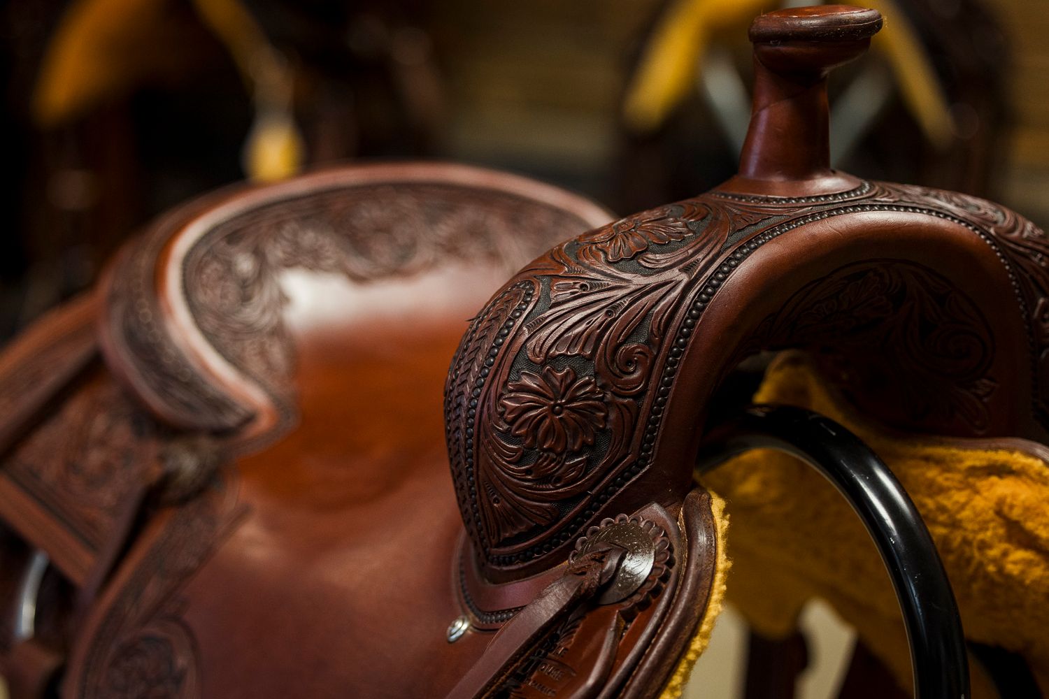 Close-up detail shot of ornate leather tooling on a brown western saddle horn showing intricate floral patterns.