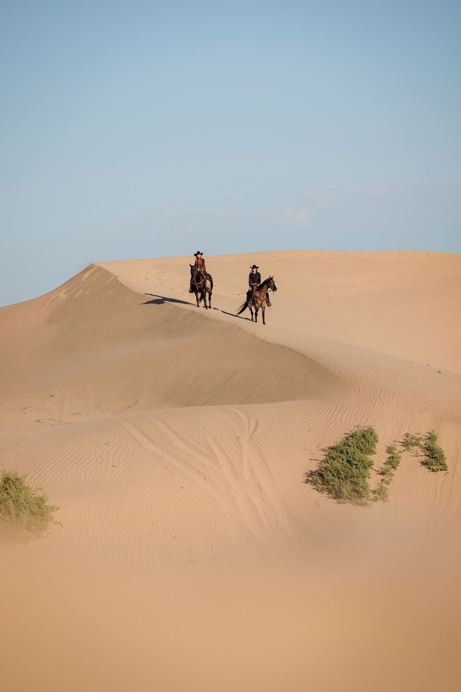 2 cowgirls on horses riding down a sand dune