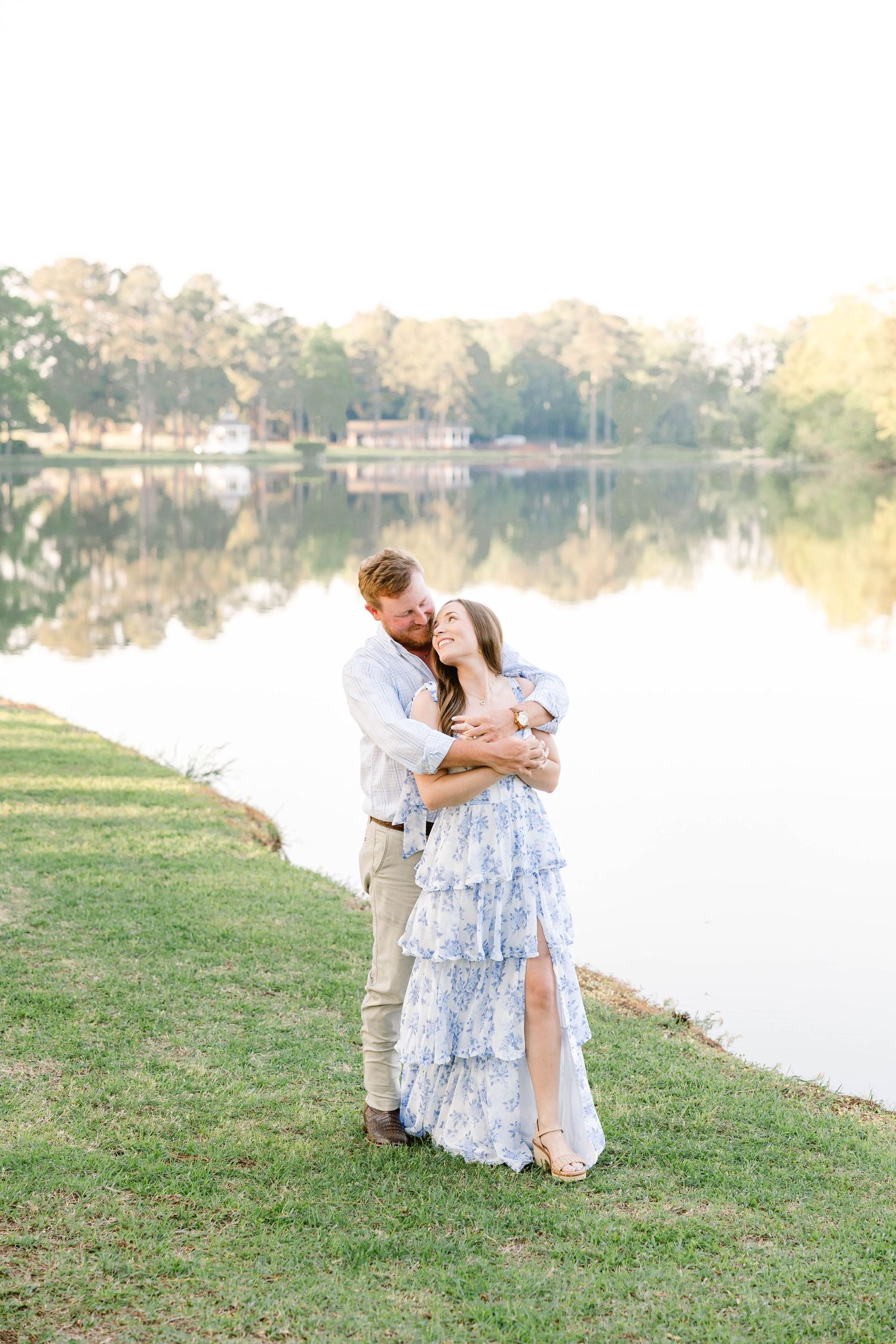 A romantic couple embracing by a serene lake during golden hour.