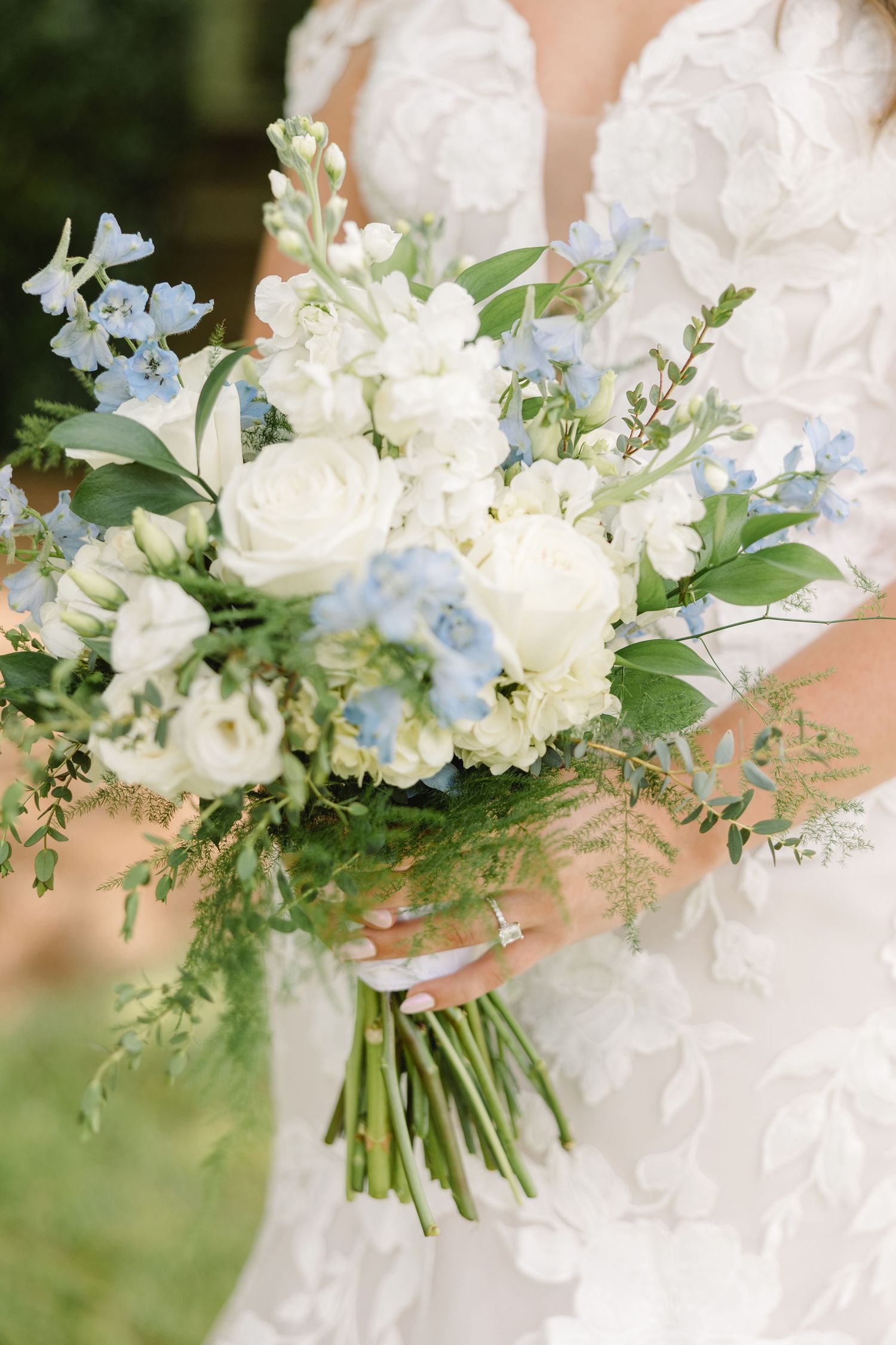 A delicate bridal bouquet featuring white roses and light blue flowers with mixed greenery.
