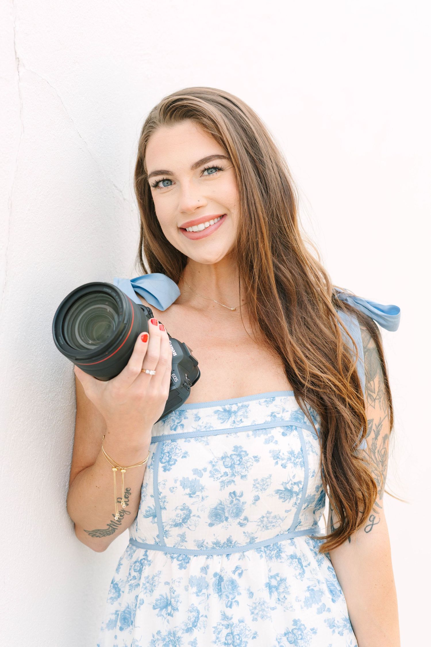 Portrait series of photographer holding camera lens while wearing blue floral dress.