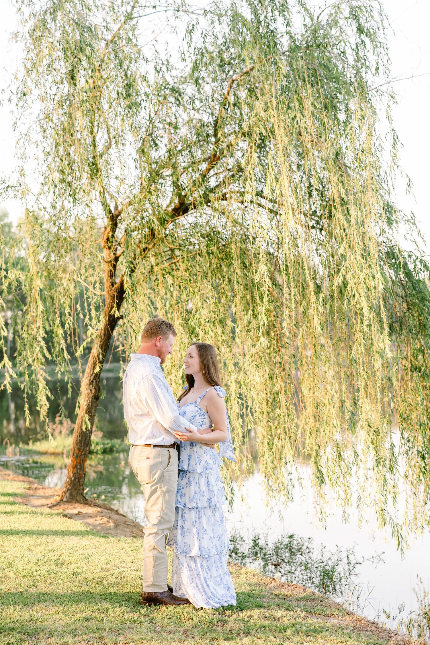 A couple sharing a romantic moment under a weeping willow tree by the water.