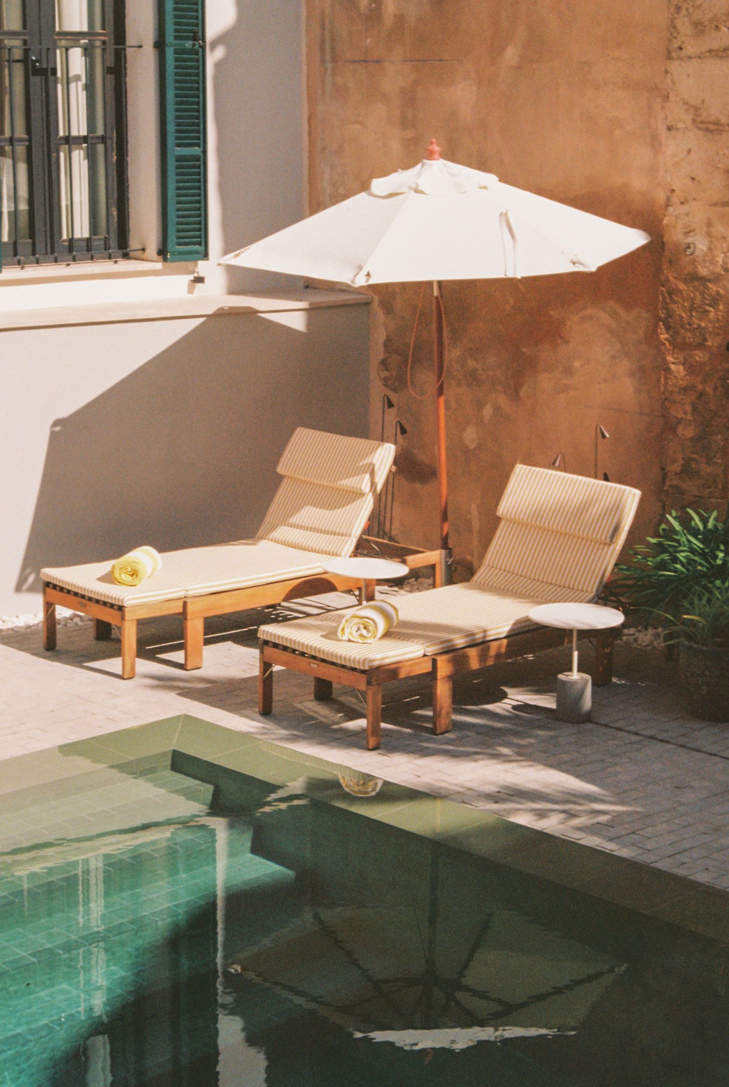 A patio area by a swimming pool. Light beige/tan colored walls and an off-white umbrella are present. 35mm shot taken in Mallorca