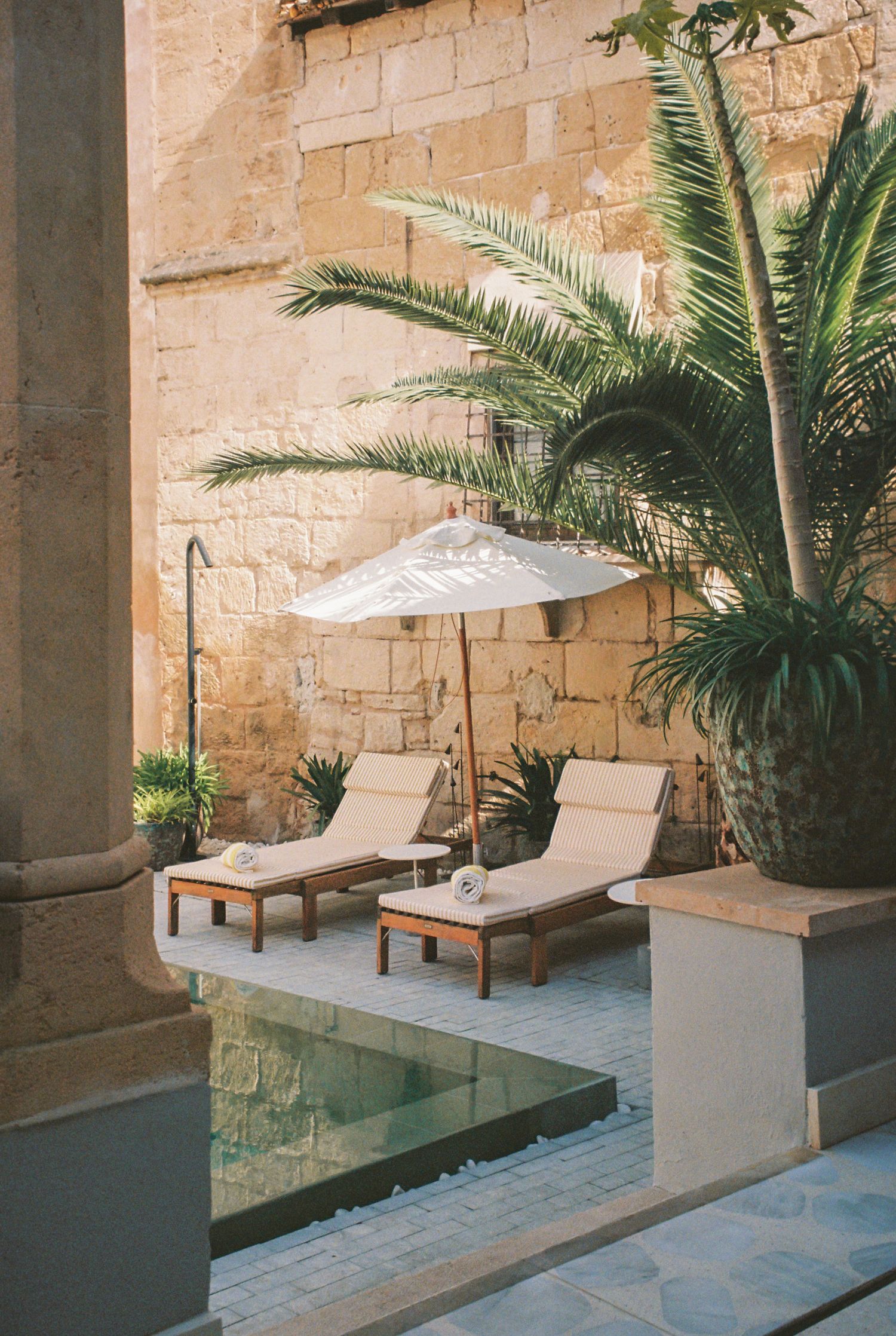 A patio area by a swimming pool. Light beige/tan colored walls and an off-white umbrella are present. 35mm shot taken in Mallorca