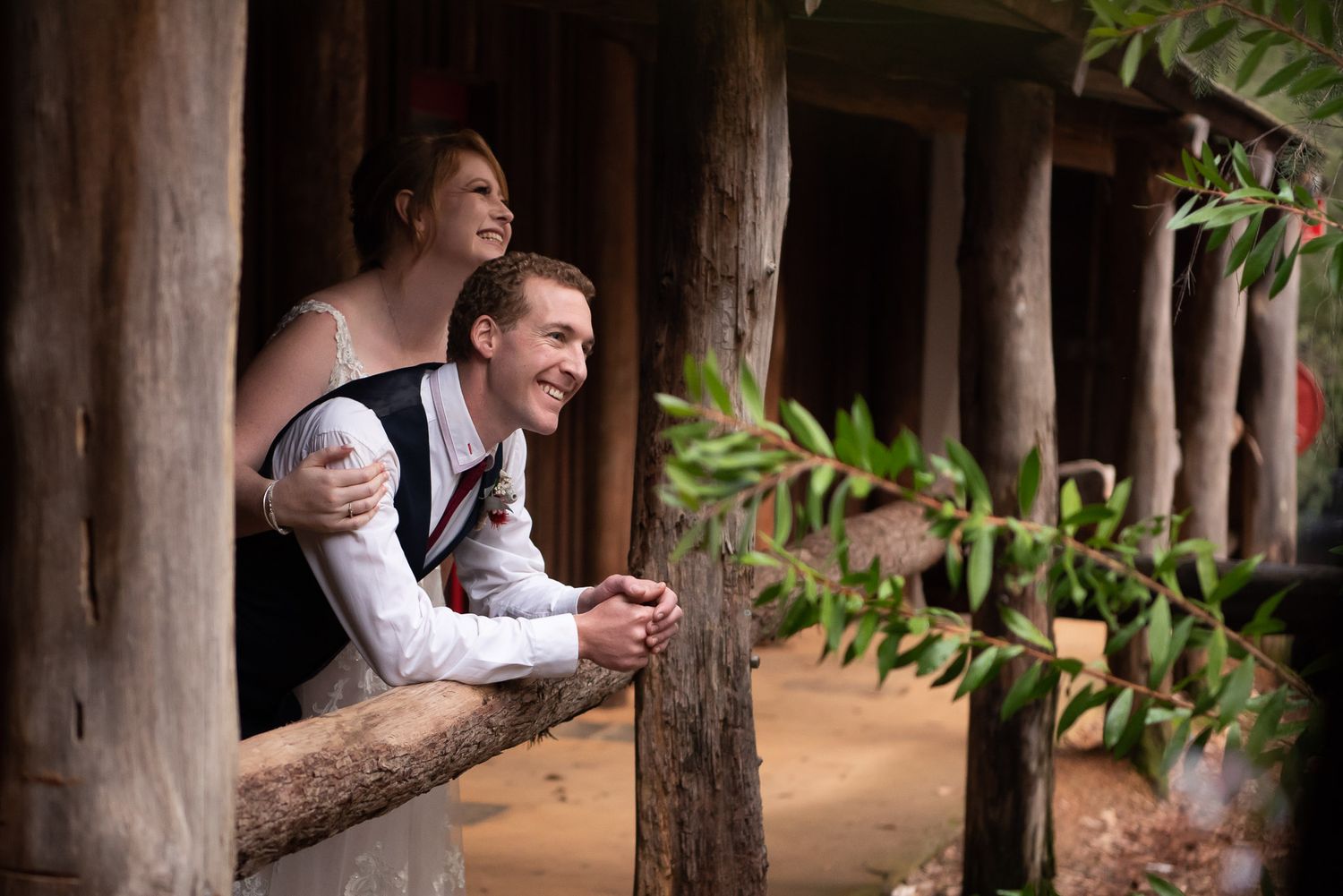 Wedding couple dressed in traditional wedding attire share a joyful moment while looking out from a rustic wooden porch at Nanga Bush Camp