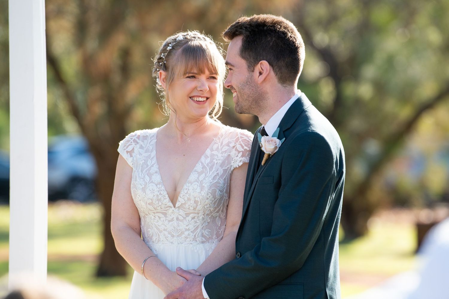 A tender moment shared between newlyweds under a white outdoor pavilion.
