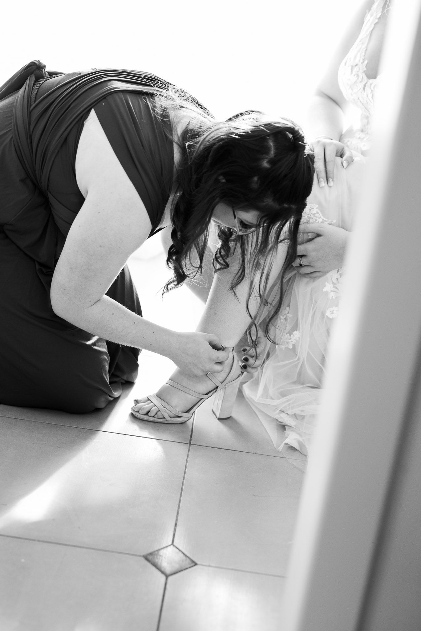 Black and white photo of someone kneeling on tiled floor examining something in dramatic lighting.