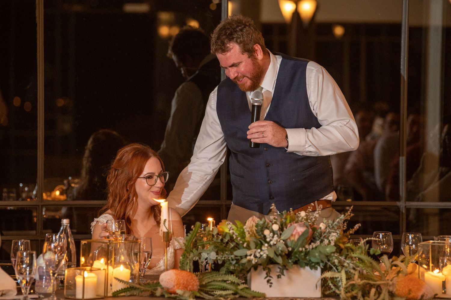 Wedding reception table decorated with greenery and candles for an evening celebration.