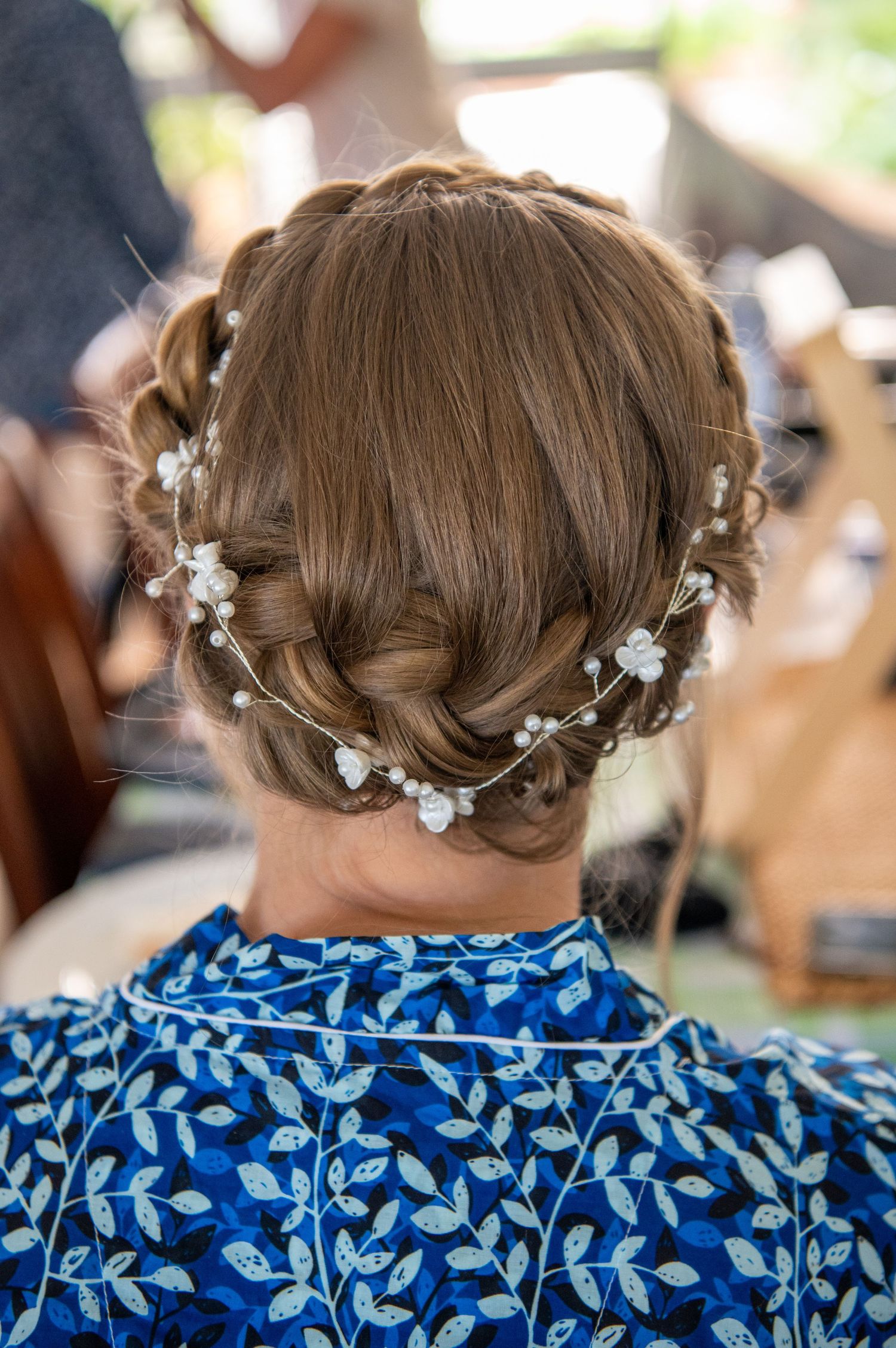 Close-up view of a bridal updo hairstyle decorated with delicate white floral accessories against a blue dress backdrop.