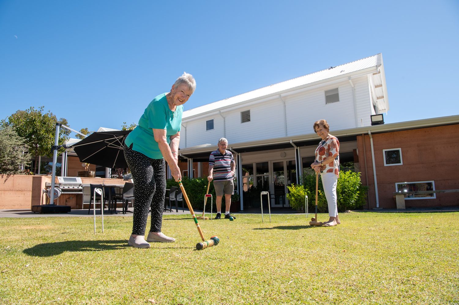 People playing mini golf on a grassy lawn outside brick buildings with various putting stances and positions.