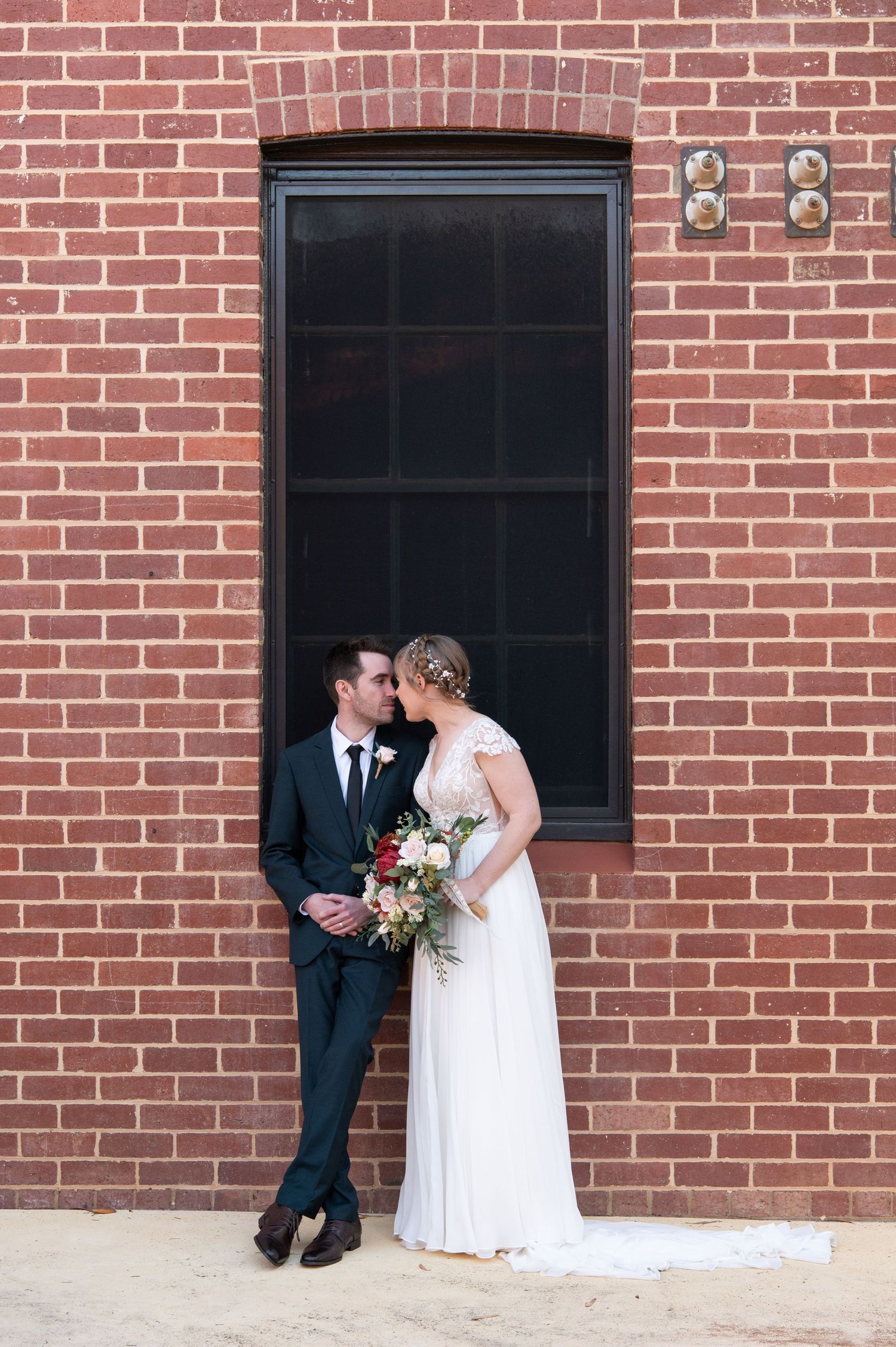 Romantic couple portrait against brick wall with large black window frame.
