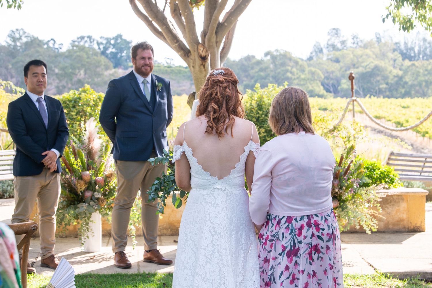 Wedding guests gathered outdoors for a celebration under trees and natural lighting.