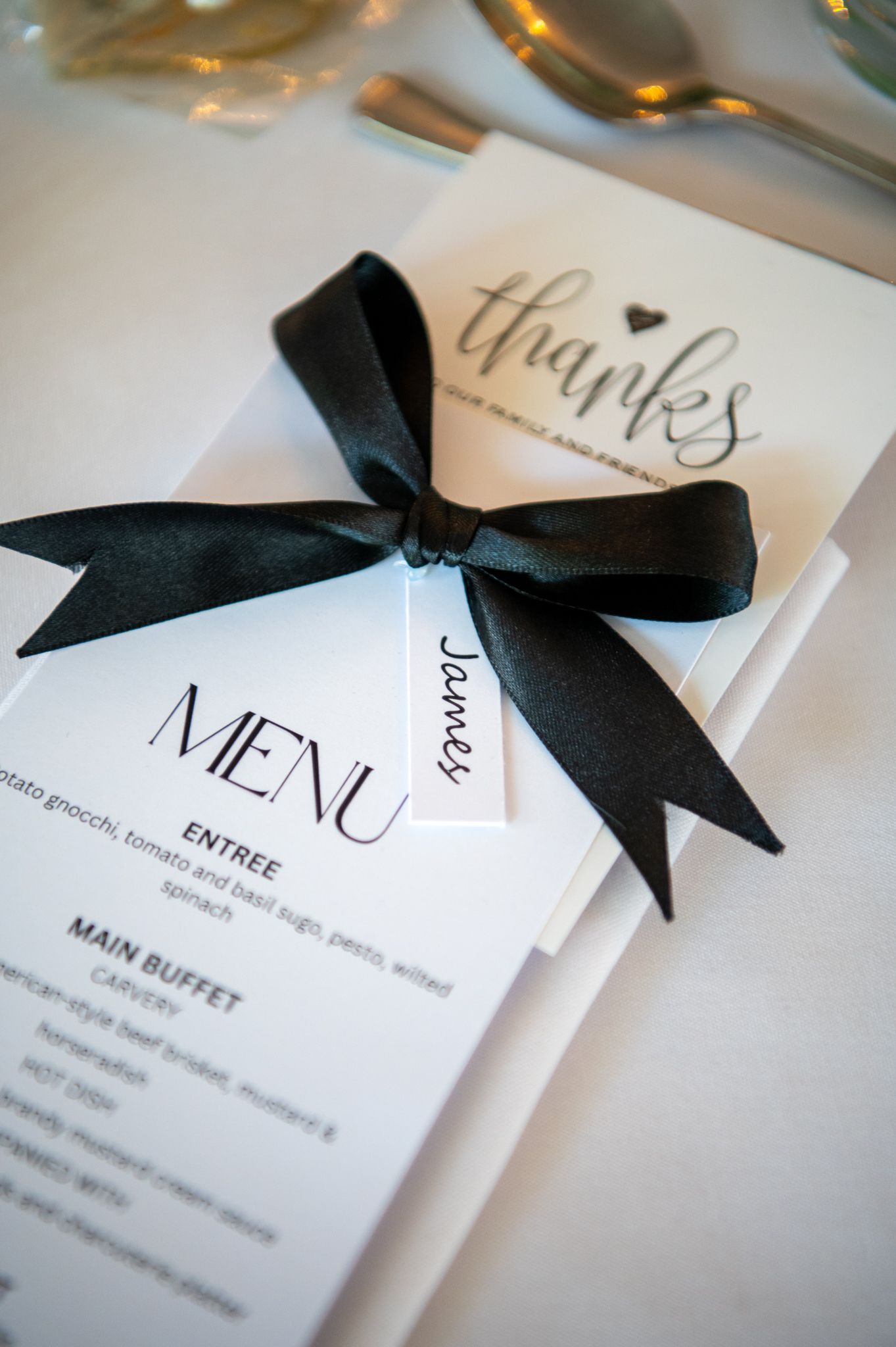 Elegant wedding menu cards decorated with black satin ribbon bows and calligraphy text sit in a row on white table.