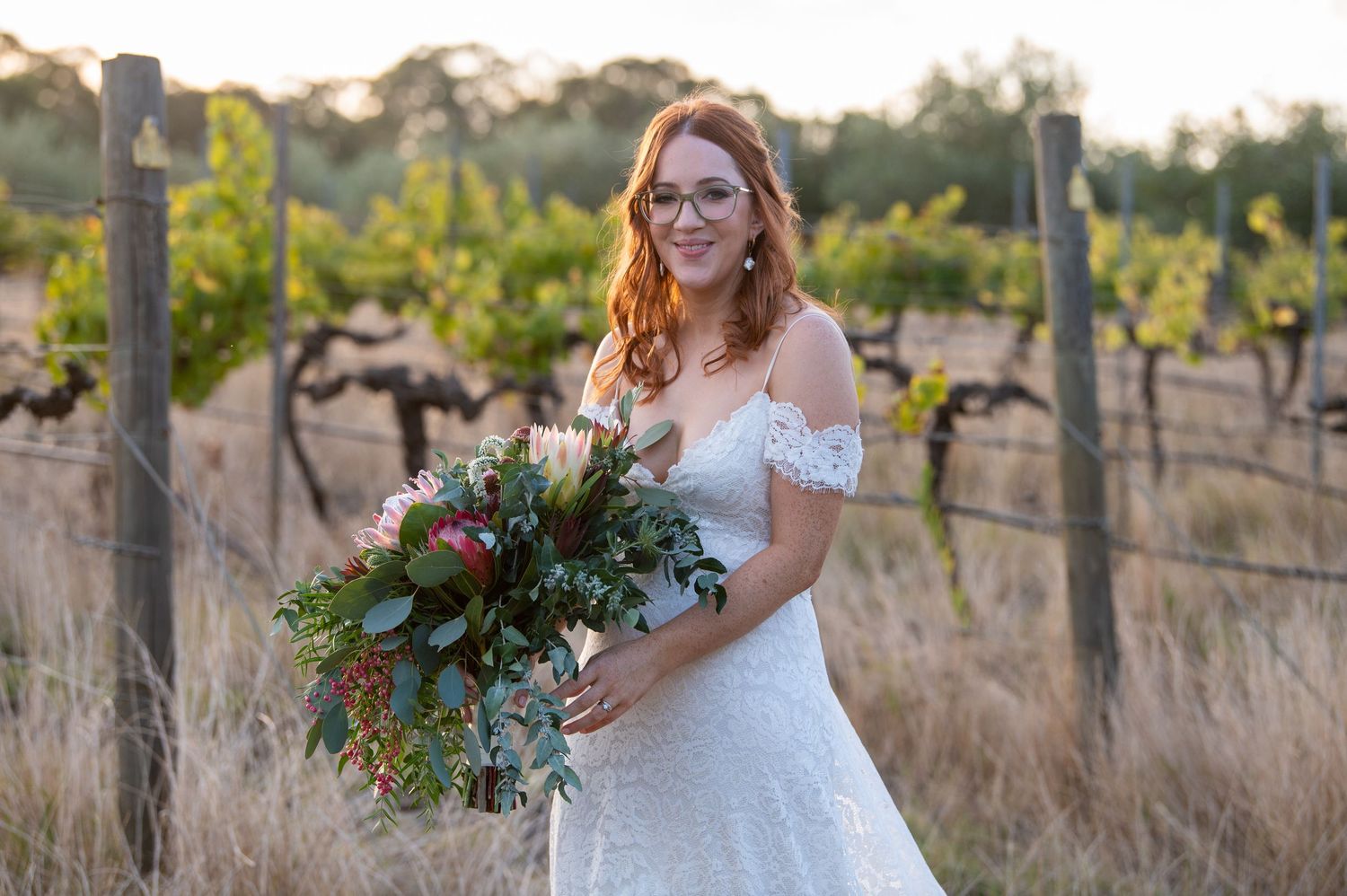A person in a wedding dress poses in a vineyard at sunset.
