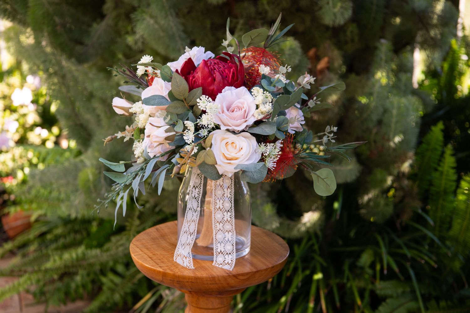 Romantic floral centerpiece with pink and burgundy roses arranged on a wooden surface in an outdoor setting.