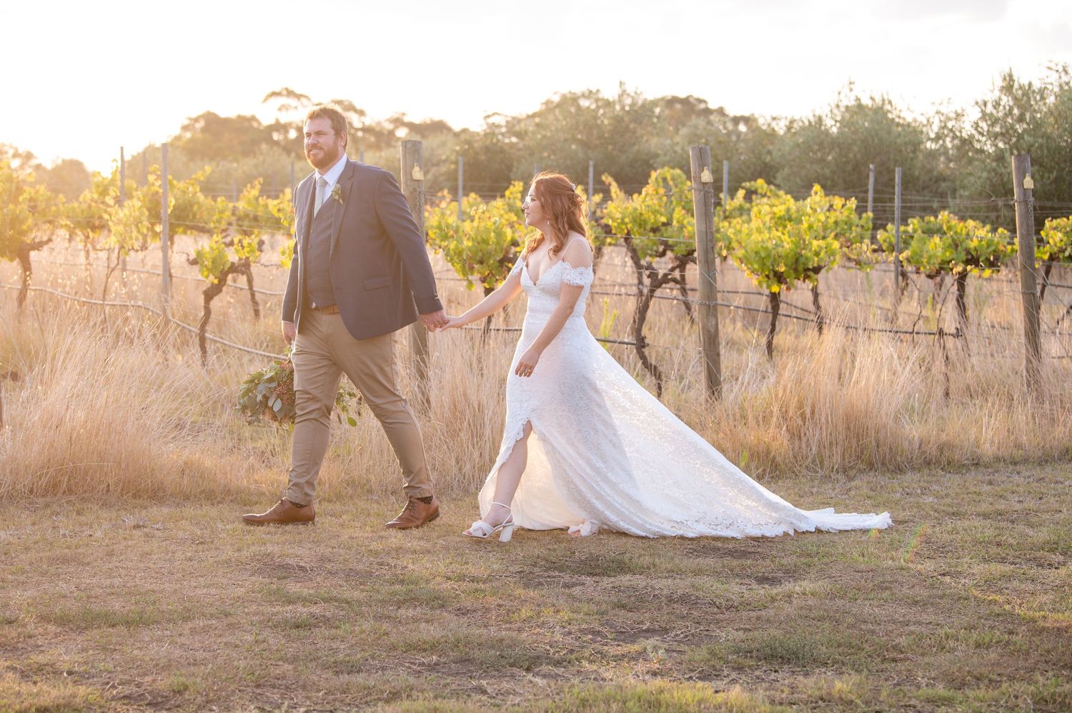Newlyweds walking through a vineyard at sunset with flowing white wedding dress.
