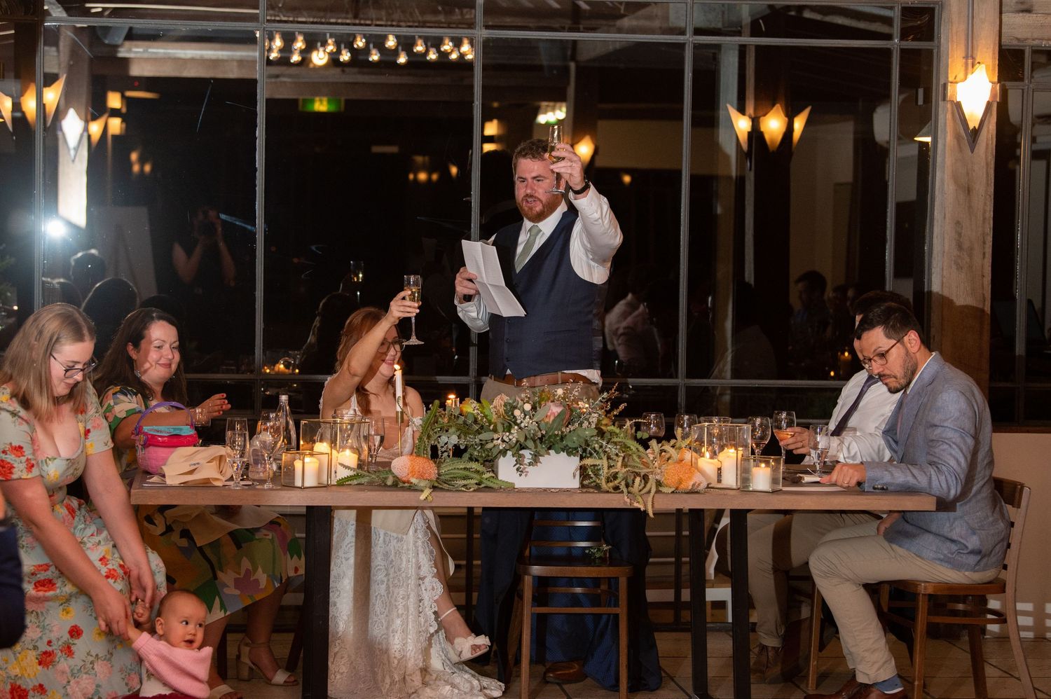 Wedding reception guests enjoying dinner while someone gives a toast.