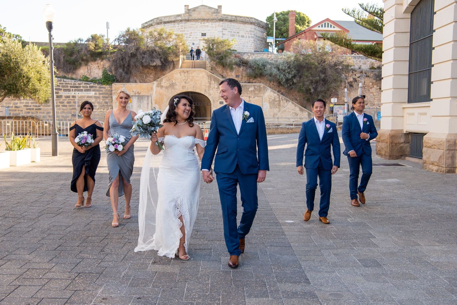 A wedding party walks together through a scenic historic courtyard on a sunny day.