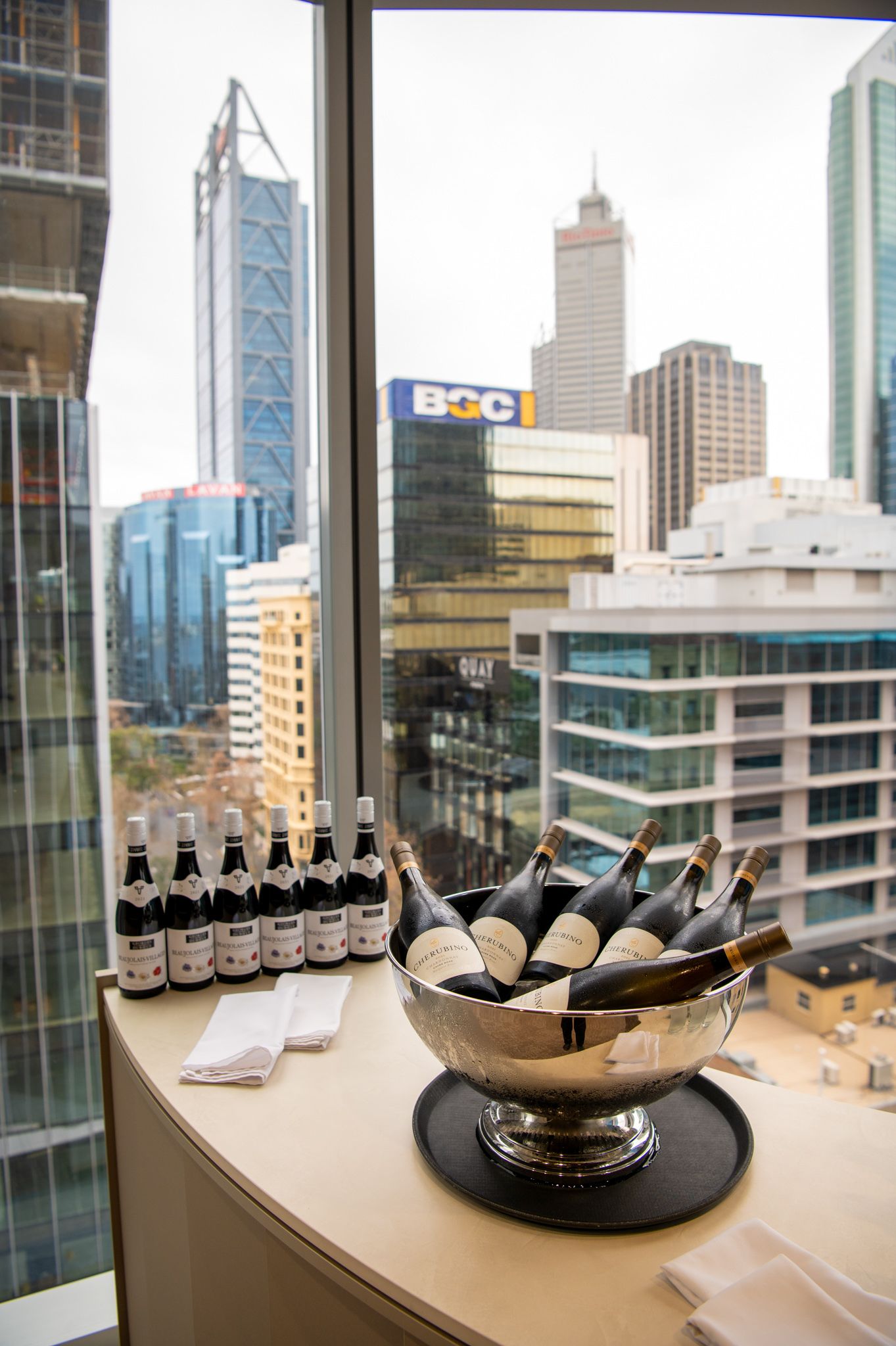 Beer bottles and oysters on ice displayed in an elegant dish with modern city skyscrapers visible through windows in background.