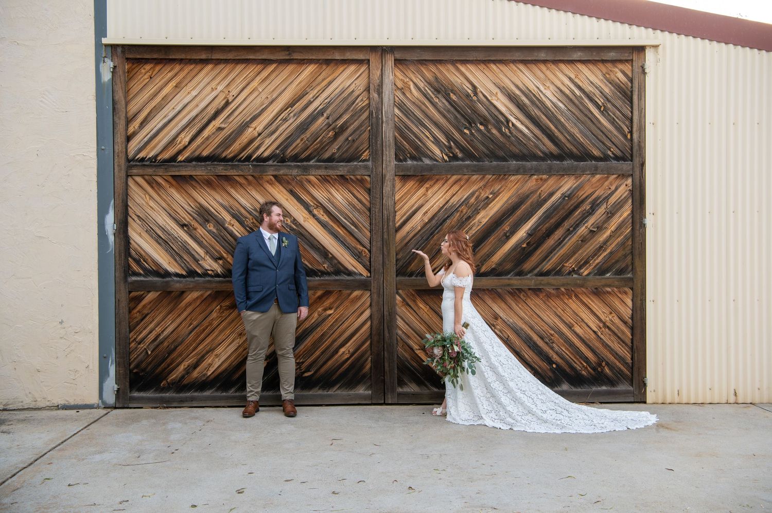 A bride and groom pose together against a rustic wooden barn door backdrop creating an elegant wedding portrait.