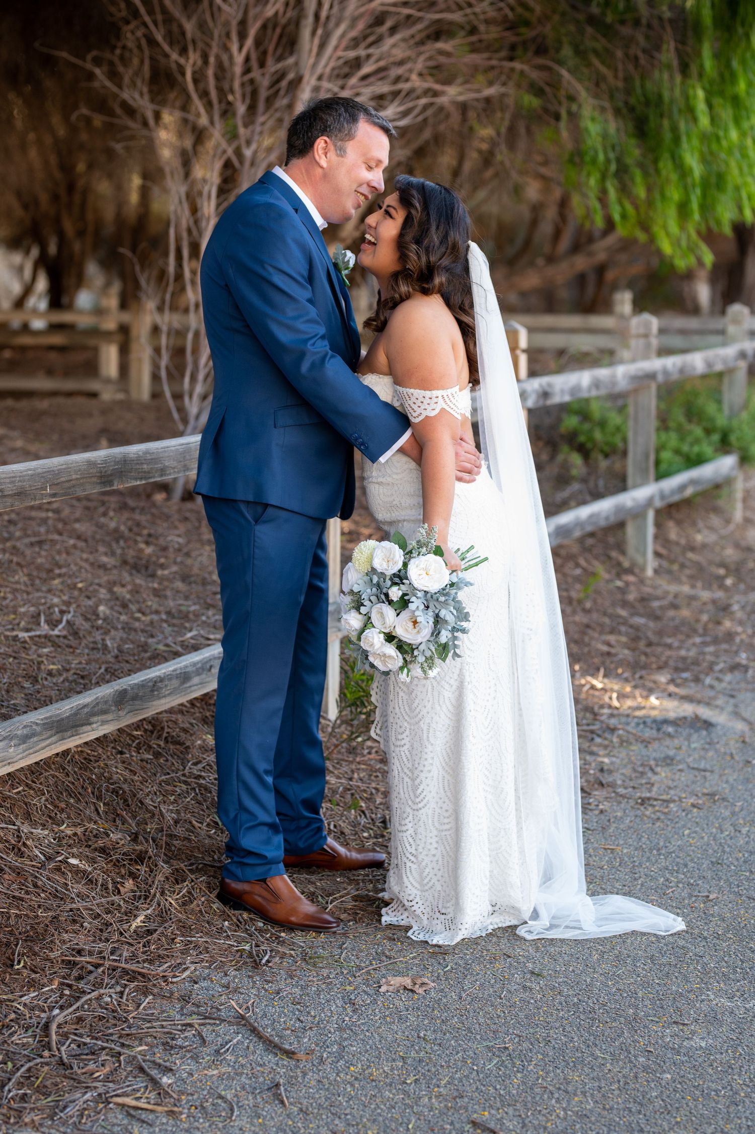 A romantic wedding portrait of a couple sharing an intimate moment along a rustic wooden fence path.