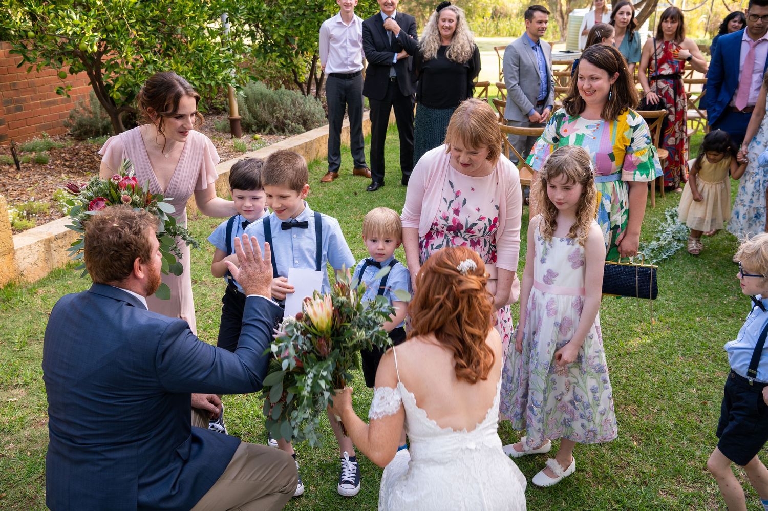 Wedding guests forming a circle on a grassy lawn during an outdoor celebration.