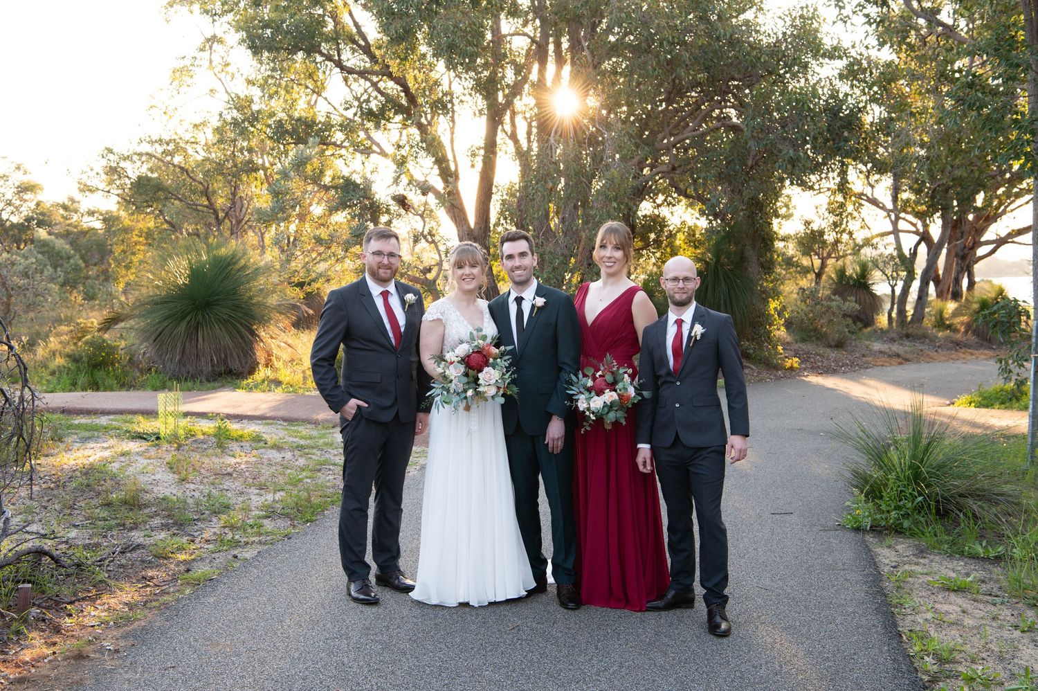 Wedding party poses together in formal attire on garden path during sunset photography session.