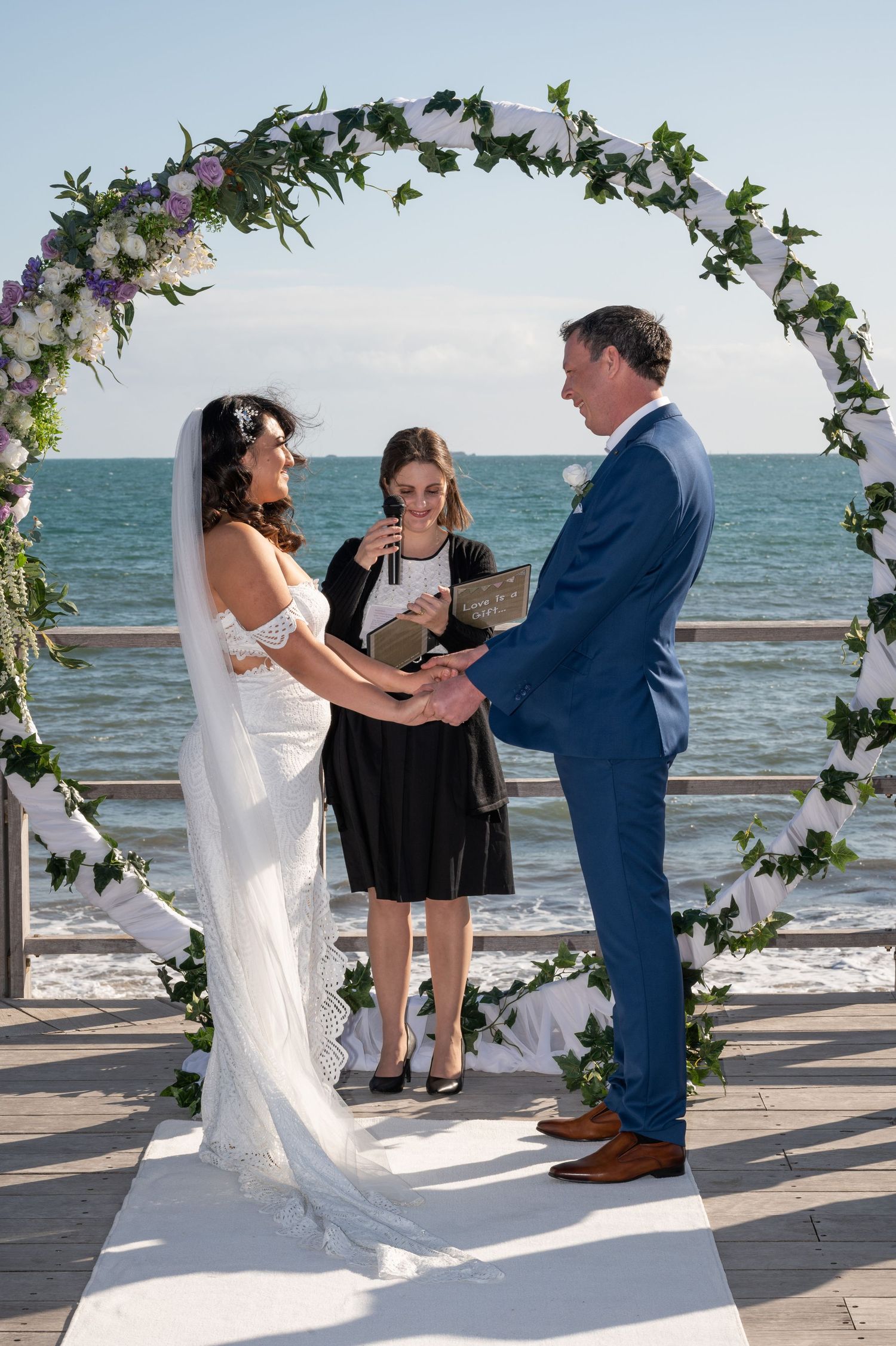 A beautiful beach wedding ceremony under a floral arch with waves crashing in the background.