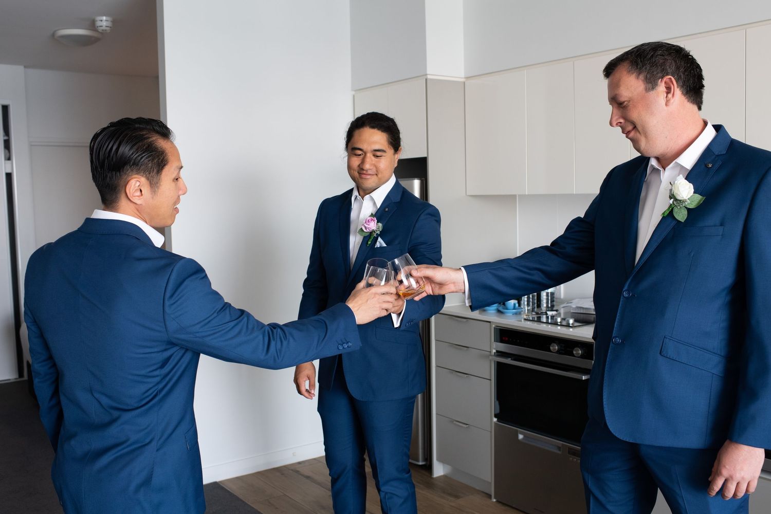 Groomsmen in navy blue suits interact and prepare in a bright hotel room before the wedding ceremony.