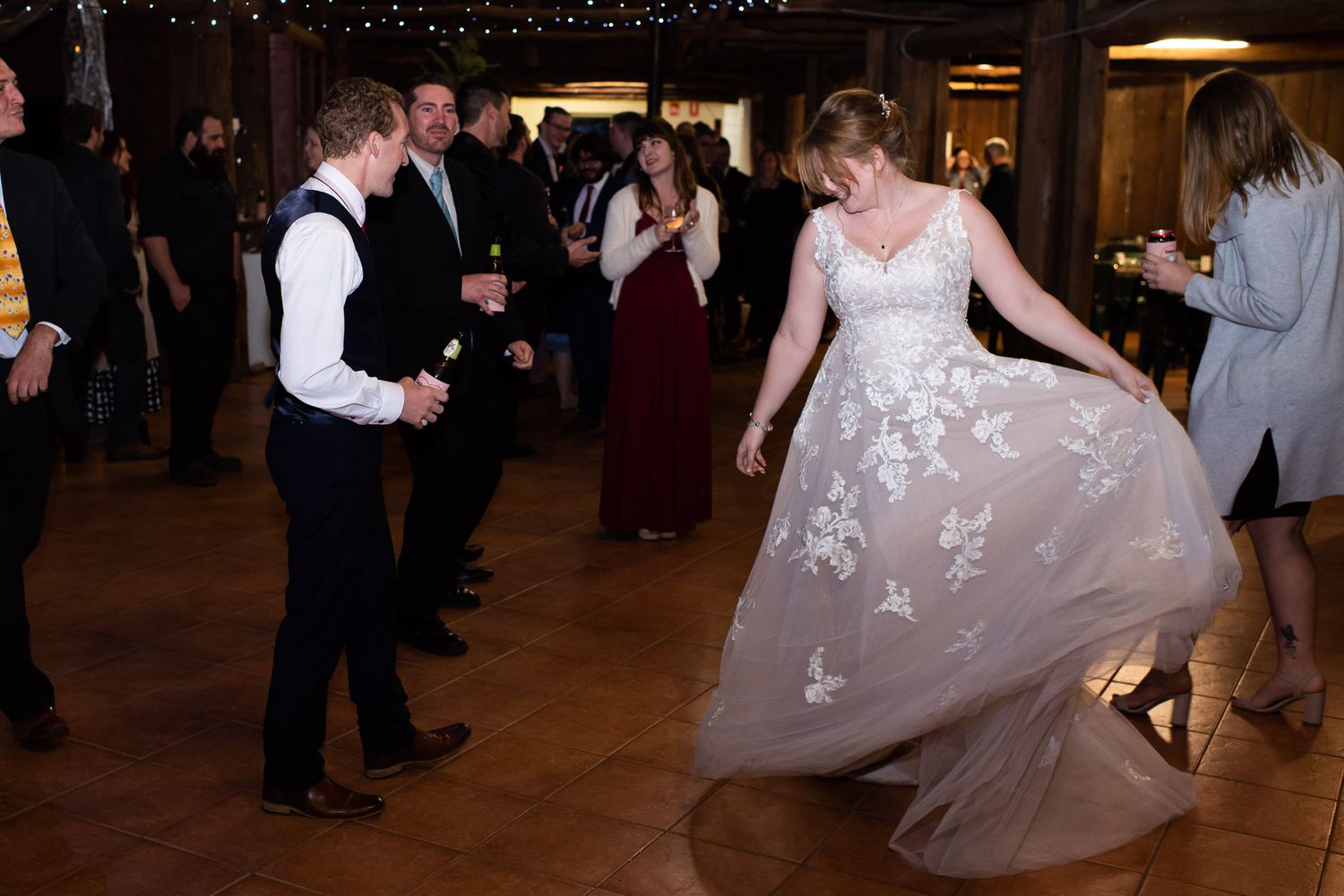 Guests dancing at a wedding reception as a bride twirls her white lace gown on the dance floor.