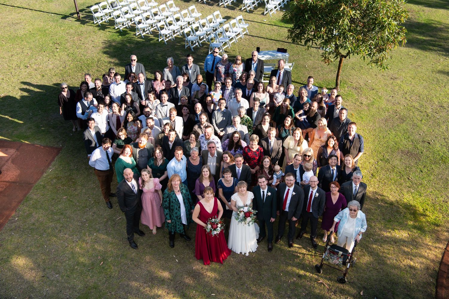 Large group wedding photo of guests and wedding party on grassy lawn.