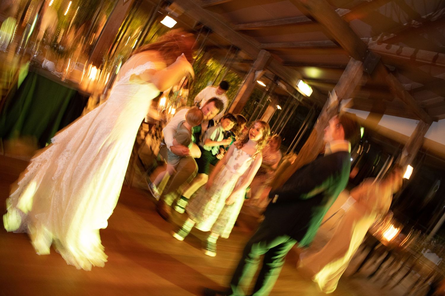 A motion-blurred scene of wedding guests dancing at an indoor reception.