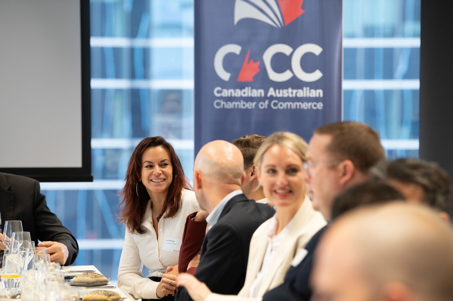 Business professionals engaged in discussion at a conference table with Canadian Australian Chamber of Commerce branding.