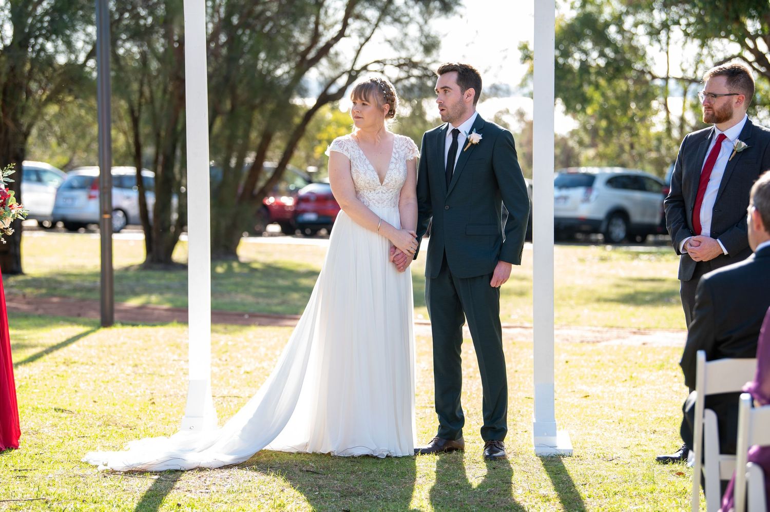 Outdoor wedding ceremony under trees with couple at altar in formal attire.