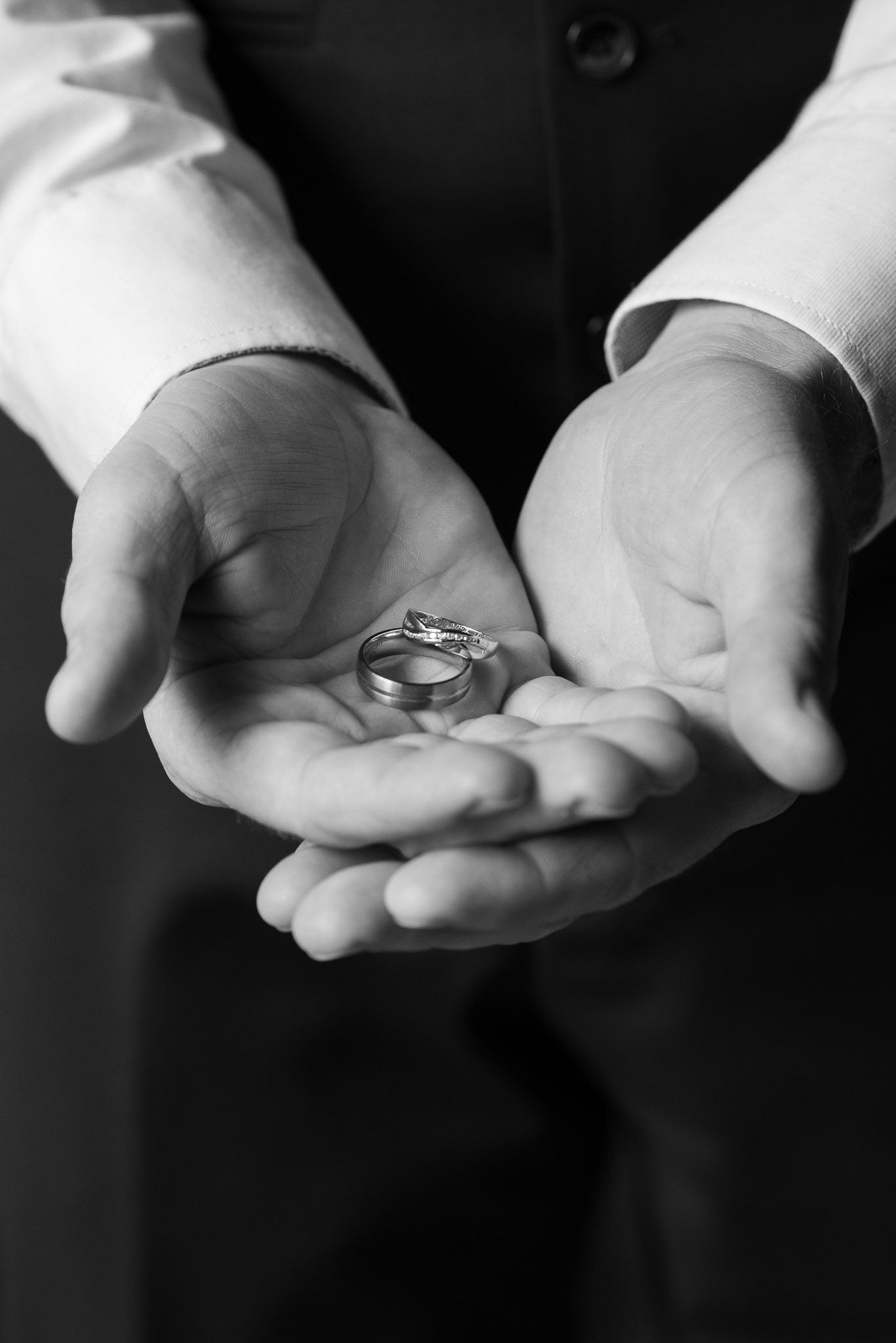 Black and white photo of hands holding wedding rings in cupped palms.