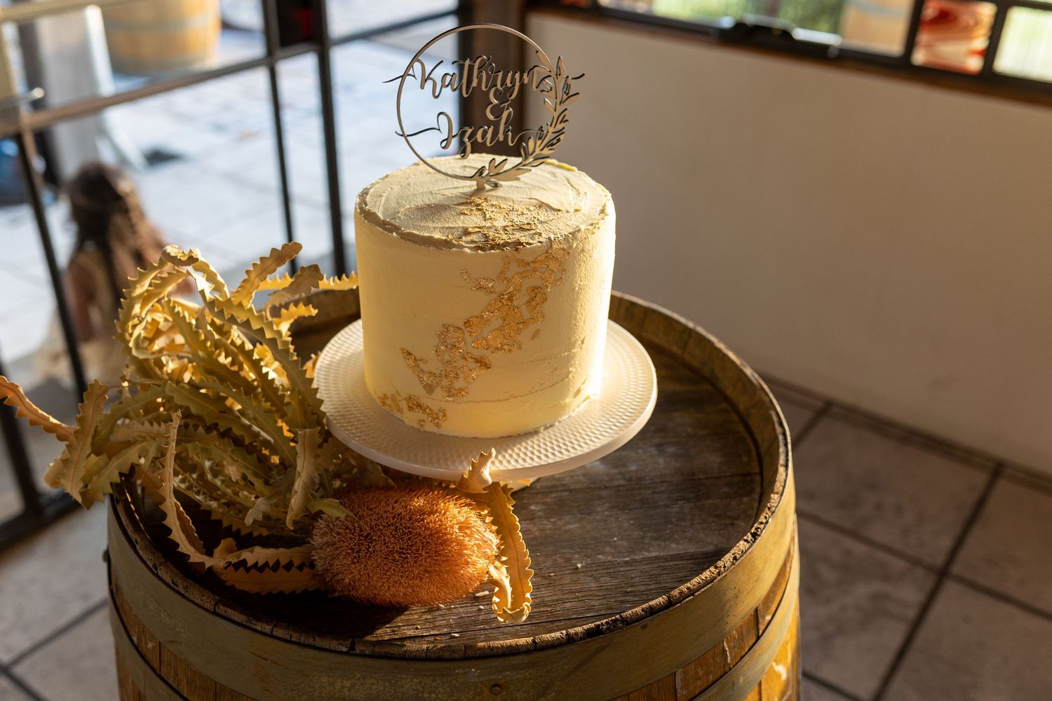 A simple elegant white and gold wedding cake displayed on a rustic barrel.