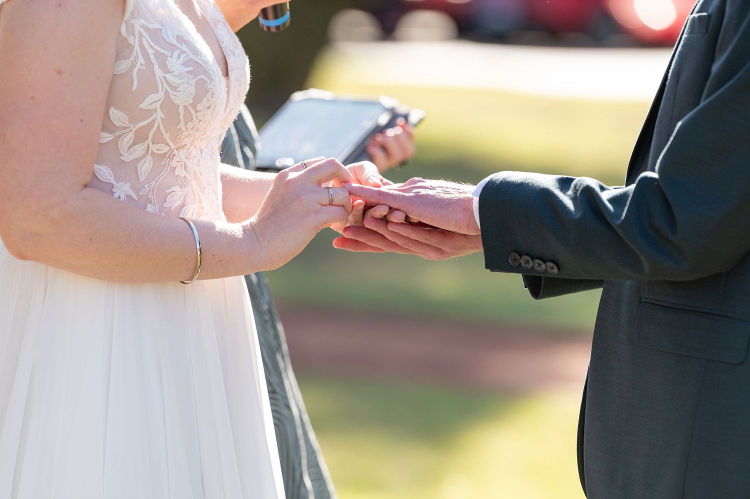A close-up shot of hands exchanging wedding rings during an outdoor ceremony.