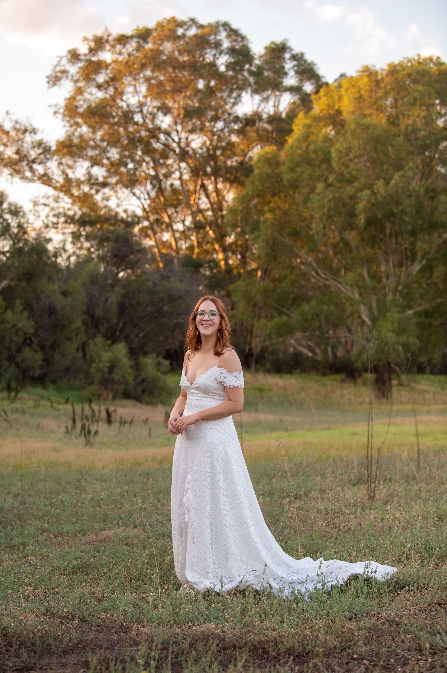 A person in a lace wedding dress poses in a golden-lit field at sunset.